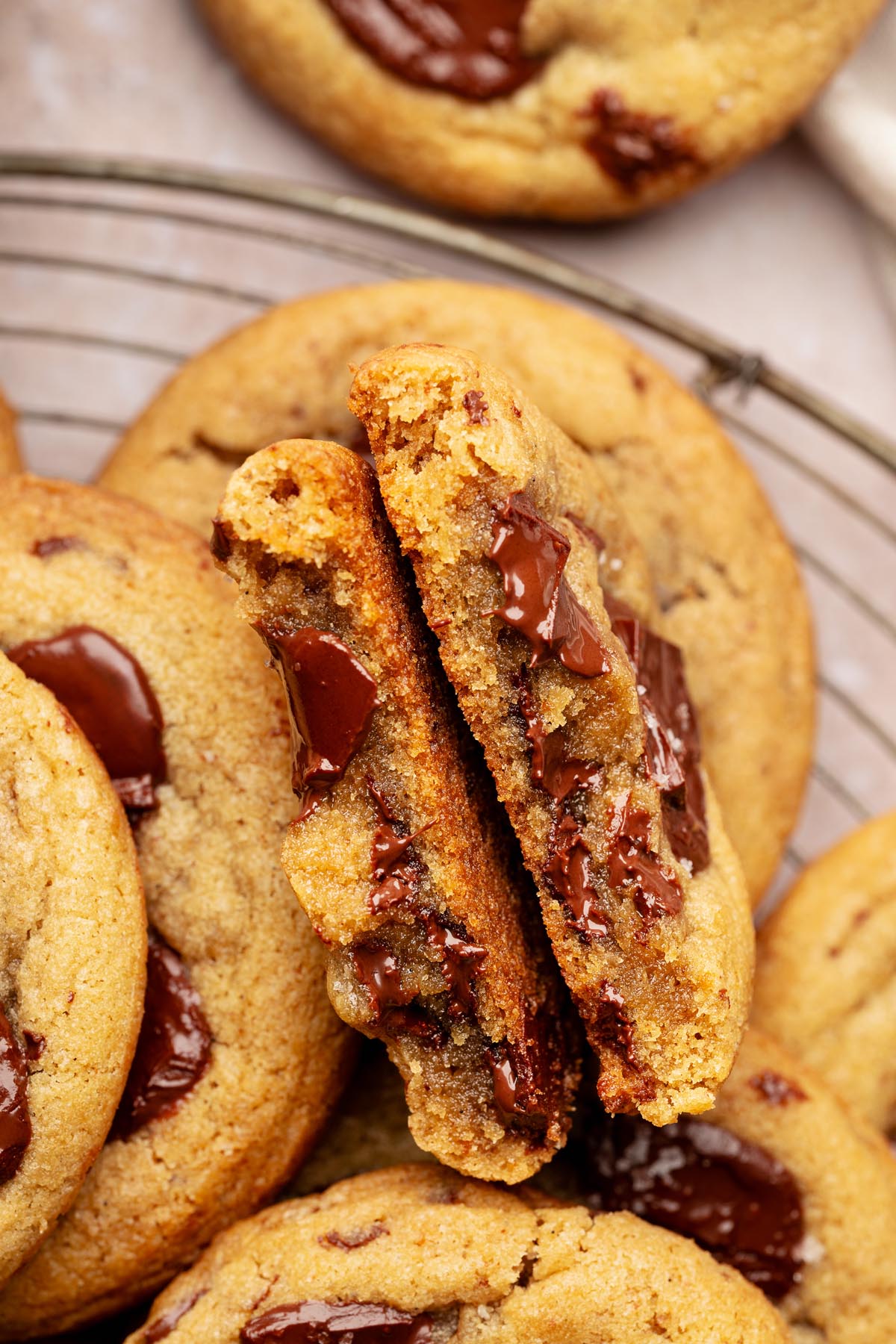 Overhead view of several golden brown chocolate chunk cookies on a cooling rack, topped with glossy melted chocolate chunks and a light sprinkle of flaky salt.