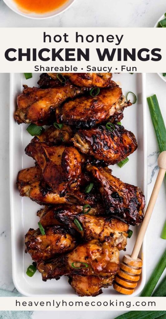 Crispy hot honey chicken wings stacked on a white platter, glazed and garnished with sliced green onions, with a honey dipper and small bowl of sauce nearby.