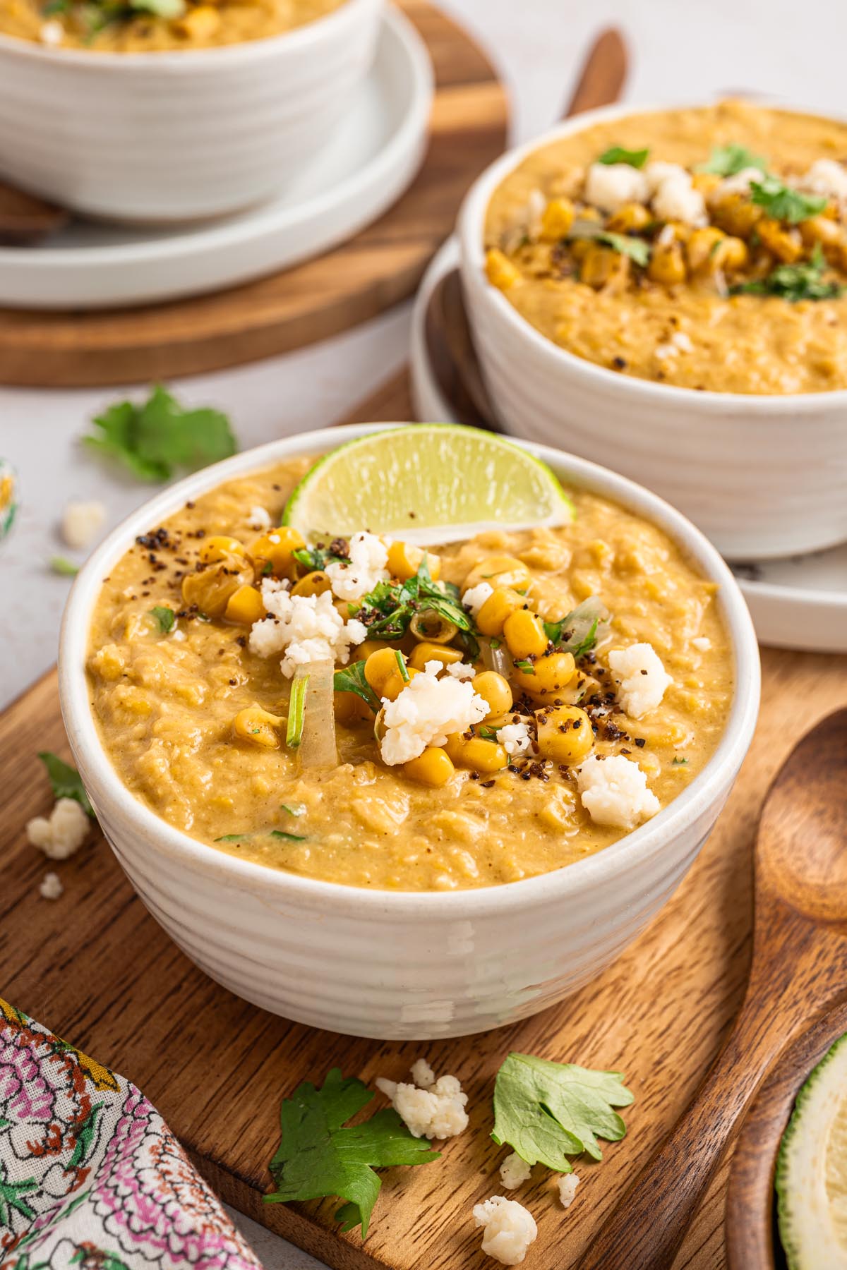 Bowl of Mexican street corn chowder garnished with corn, cilantro, Cotija cheese, and a lime wedge, with additional bowls of chowder in the background.