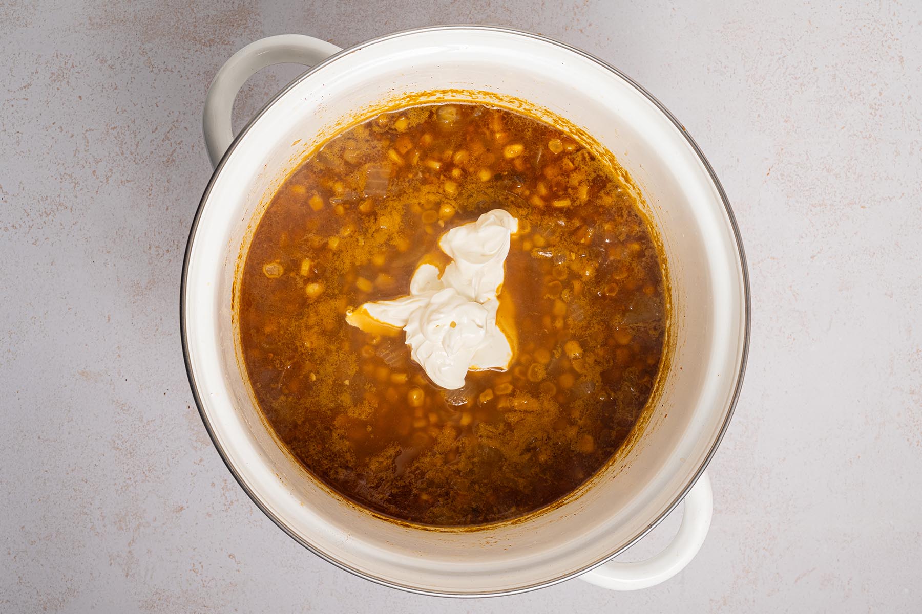 Pot of Mexican street corn chowder with a dollop of sour cream added to the center before stirring.