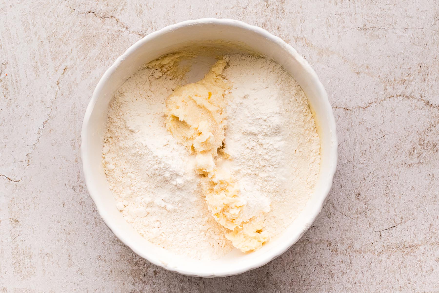 All-purpose flour added to creamed butter and sugar in a mixing bowl before being mixed into cookie dough.