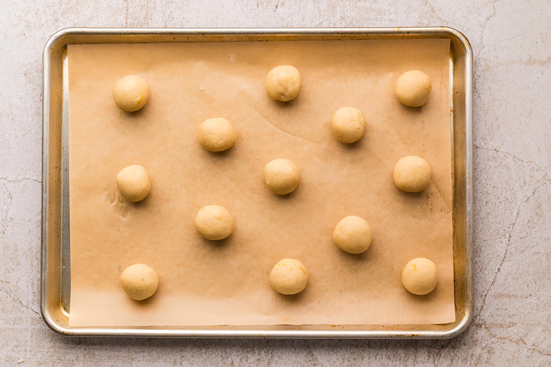 Smooth cookie dough rolled into evenly sized balls and spaced on a parchment-lined baking sheet.
