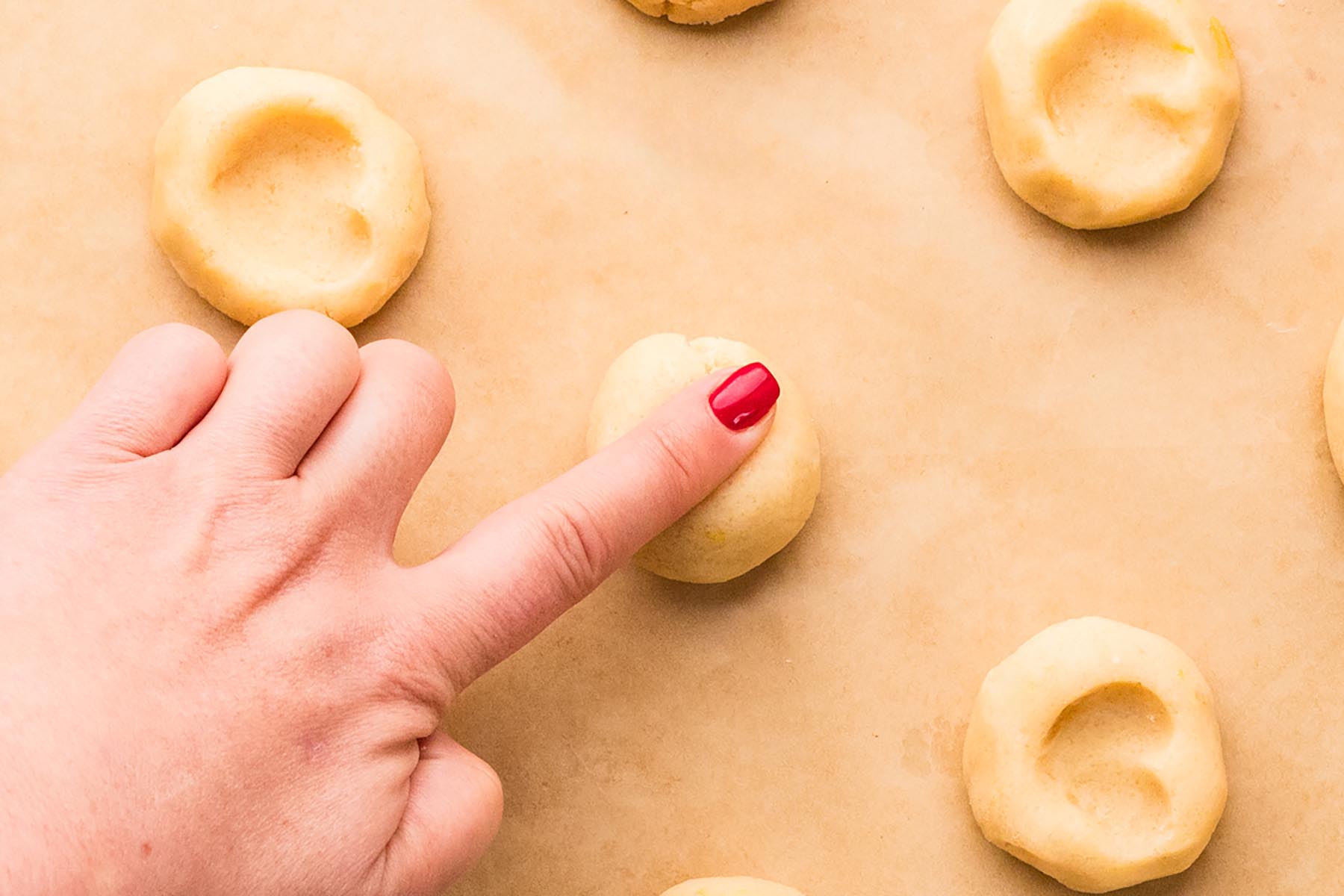 A finger pressing an indentation into a ball of cookie dough to shape thumbprint cookies.