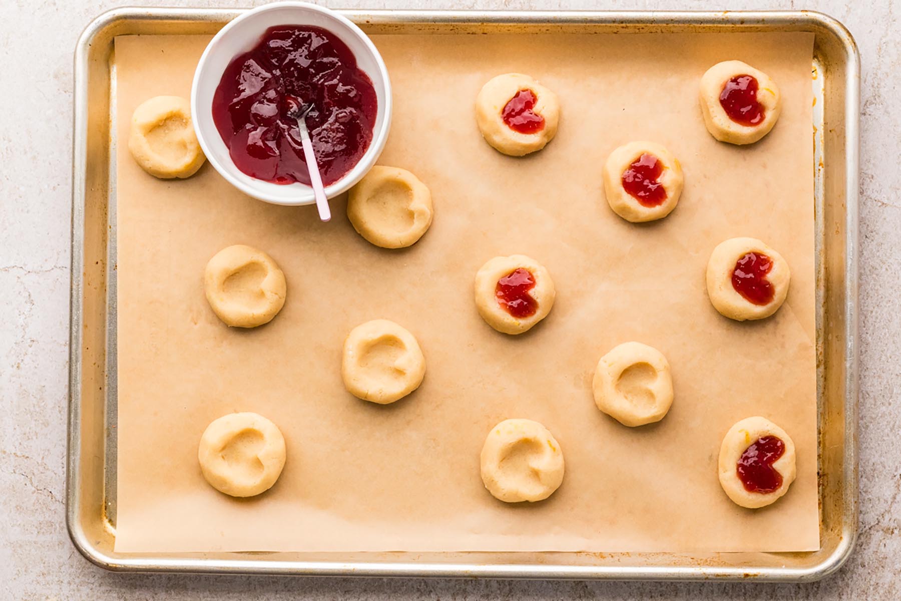 Thumbprint cookies with indentations formed and arranged on a parchment-lined baking sheet before filling.