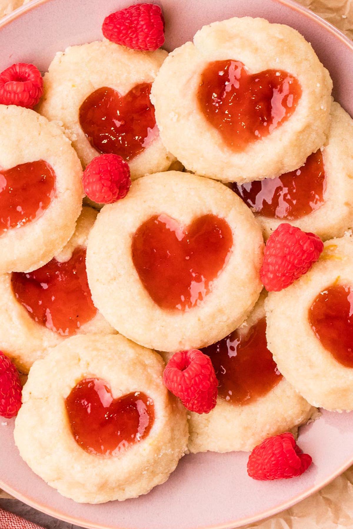 Close-up of heart-shaped raspberry thumbprint cookies with glossy jam centers.