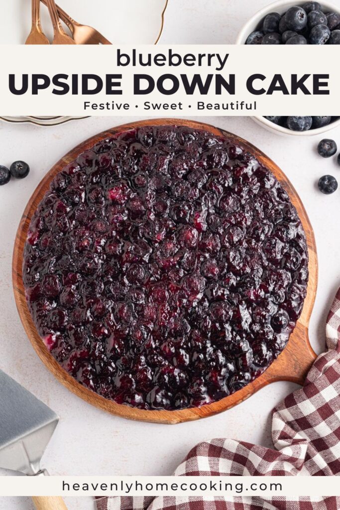Overhead view of a blueberry upside down cake with a glossy blueberry topping on a wooden serving board, surrounded by fresh blueberries and kitchen linens, with text overlay reading “Blueberry Upside Down Cake.”
