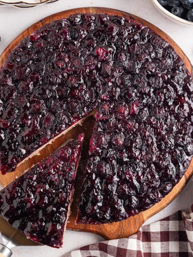 Overhead view of a blueberry upside-down cake with one slice lifted on a cake server, showing the glossy blueberry topping.