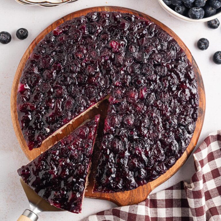 Overhead view of a blueberry upside-down cake with one slice lifted on a cake server, showing the glossy blueberry topping.