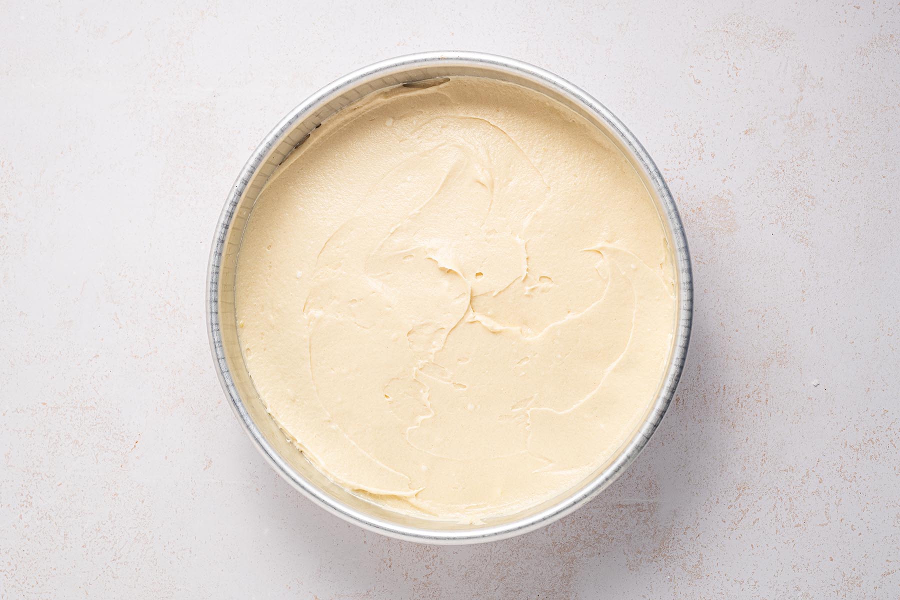 Cake batter spread evenly in a round cake pan before baking.