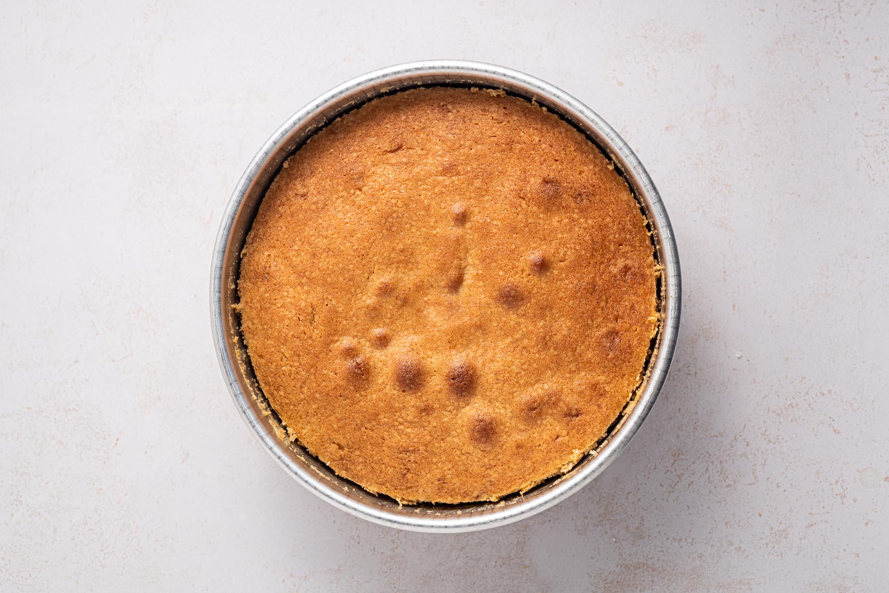 Freshly baked cake with a golden brown top in a round pan.