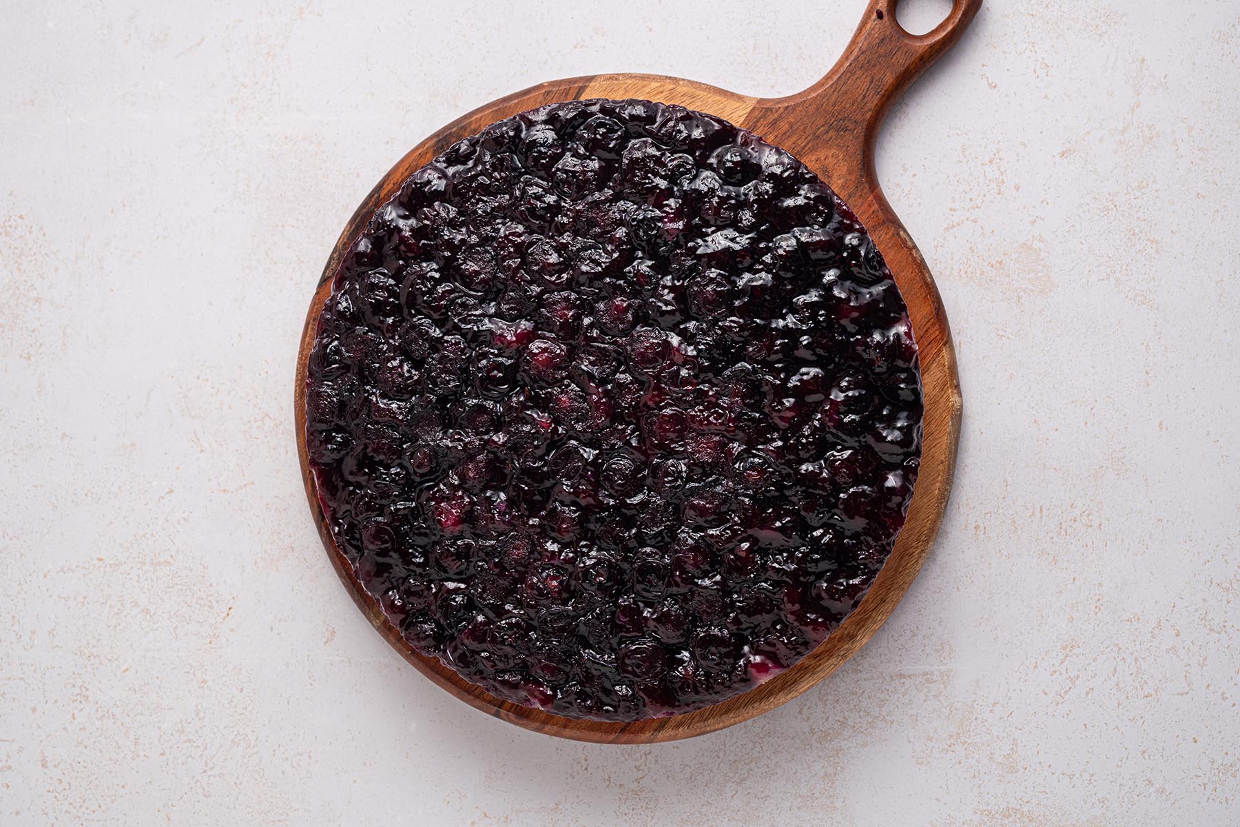 Blueberry cake inverted onto a wooden serving board with glossy fruit topping.