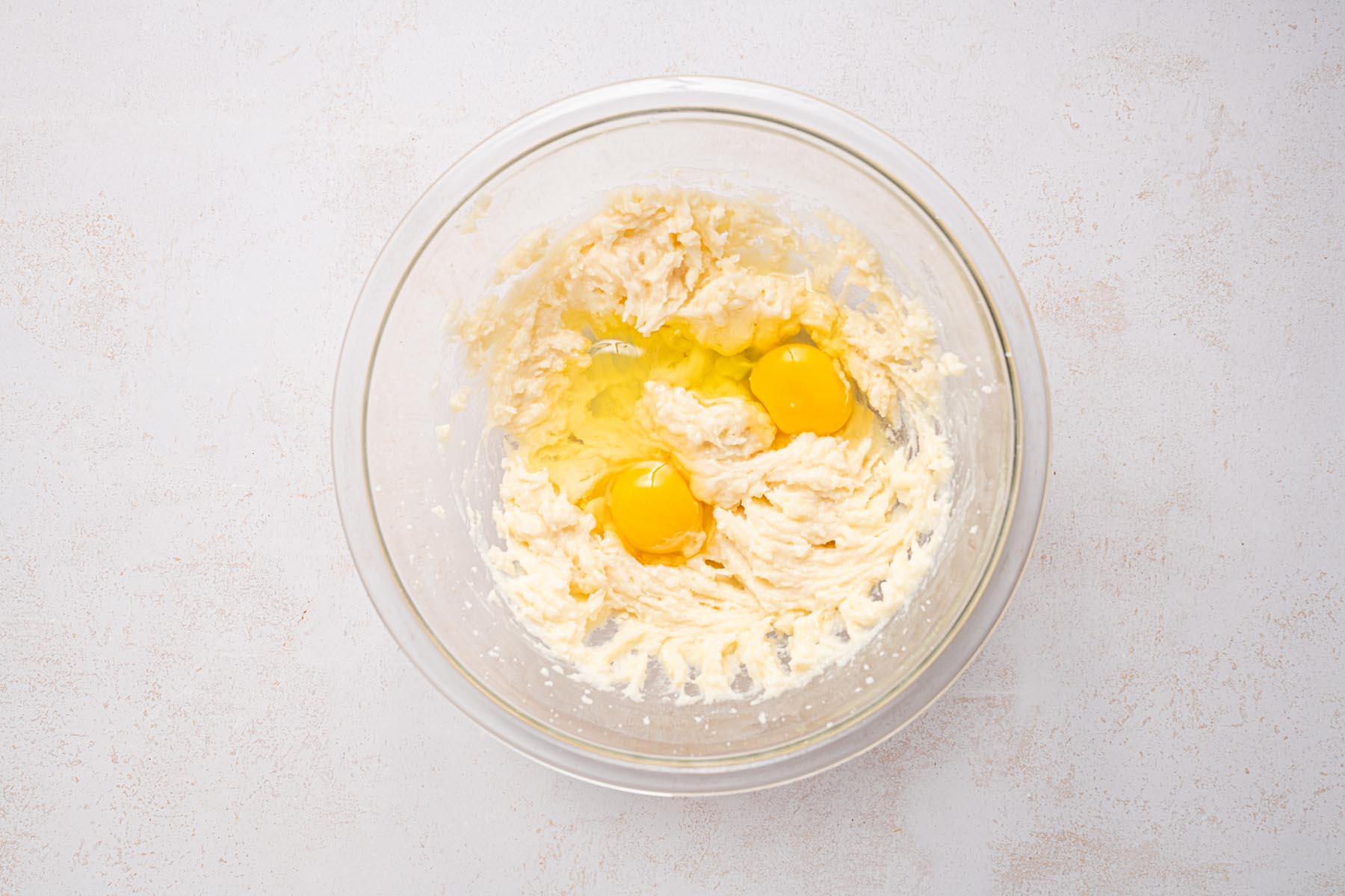 Eggs added to creamed butter mixture in a glass bowl.