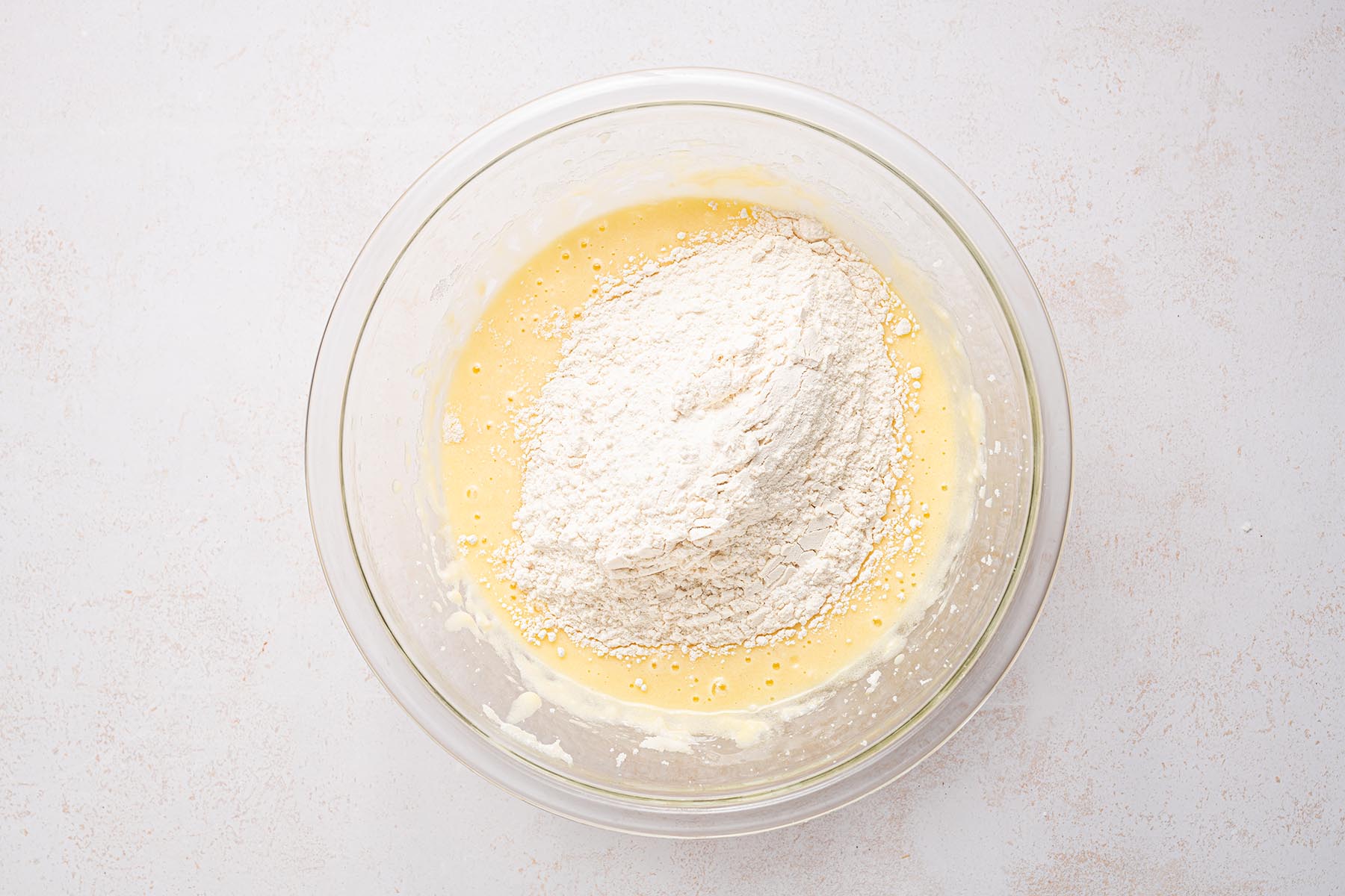 Dry ingredients added to wet ingredients in a glass mixing bowl.