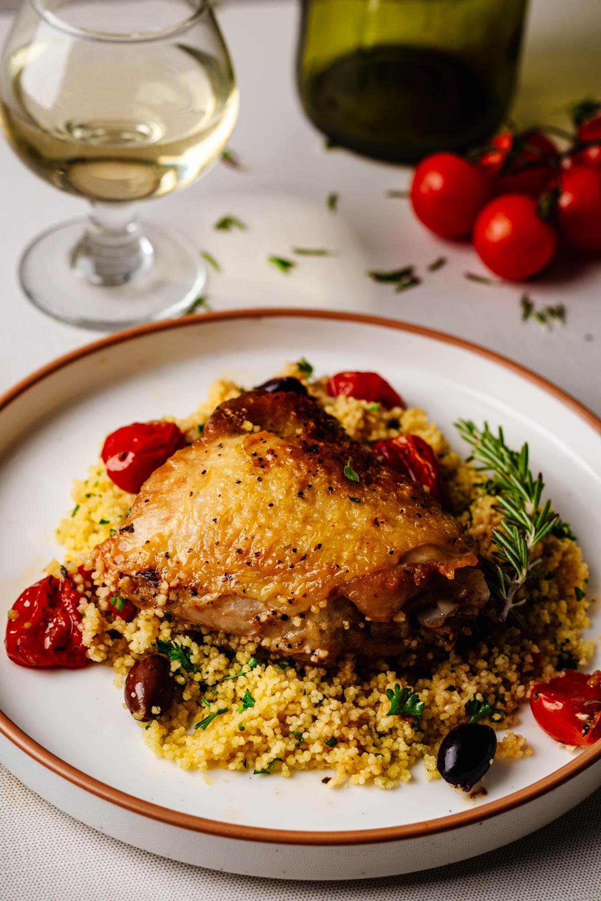 Chicken Proven&ccedil;al served over couscous with roasted tomatoes, olives, rosemary, and a glass of white wine.