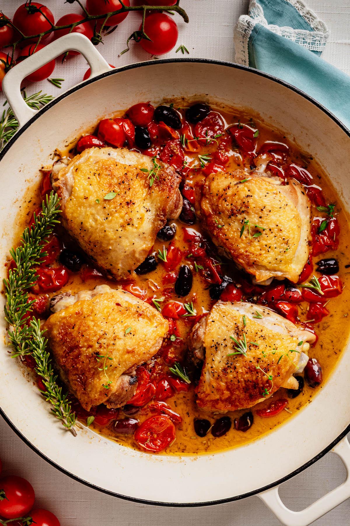 Golden roasted chicken thighs in a skillet with cherry tomatoes, olives, rosemary, and savory pan sauce.