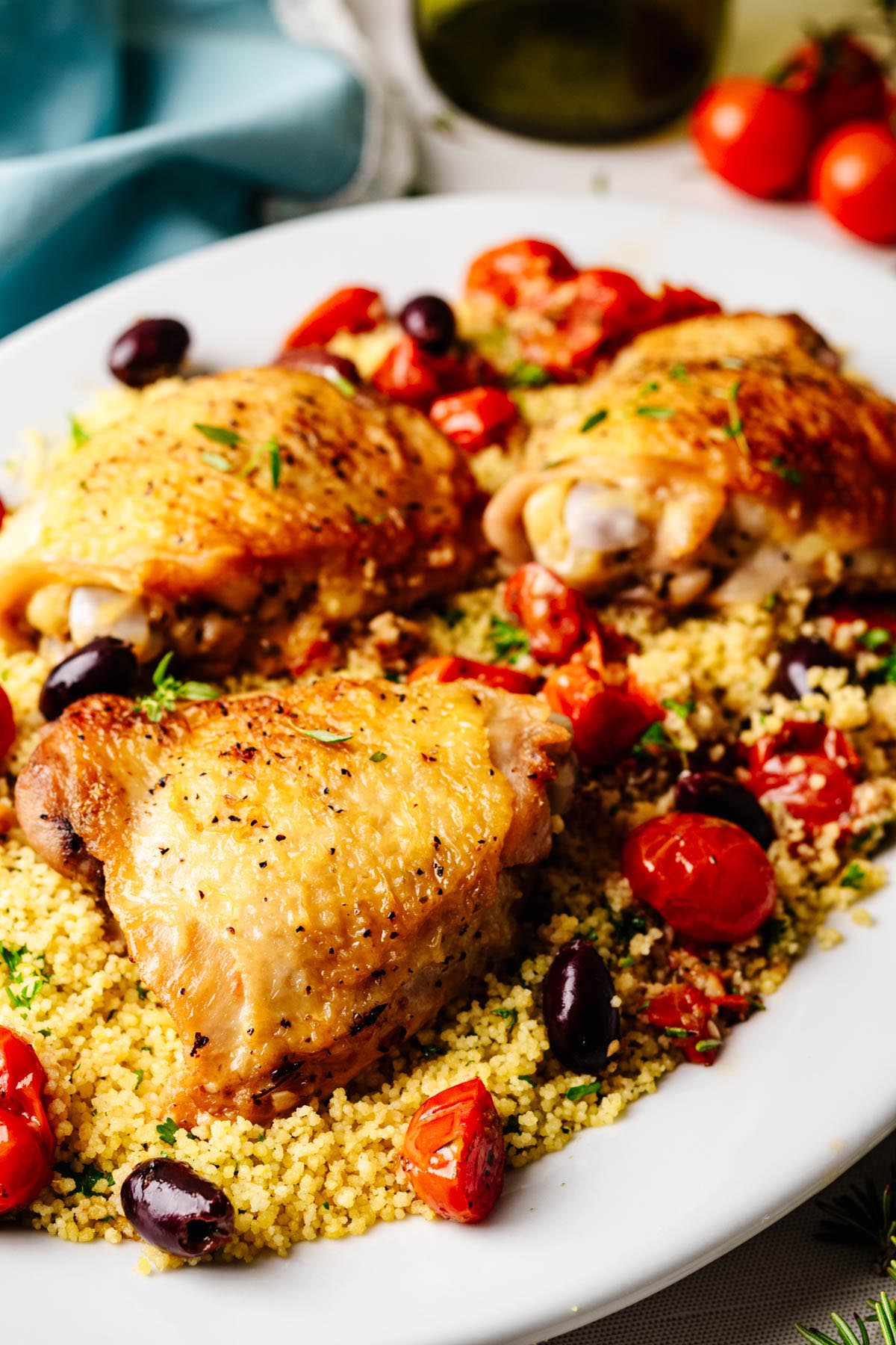 Close-up of crispy roasted chicken thighs over couscous with roasted tomatoes, olives, and fresh herbs.