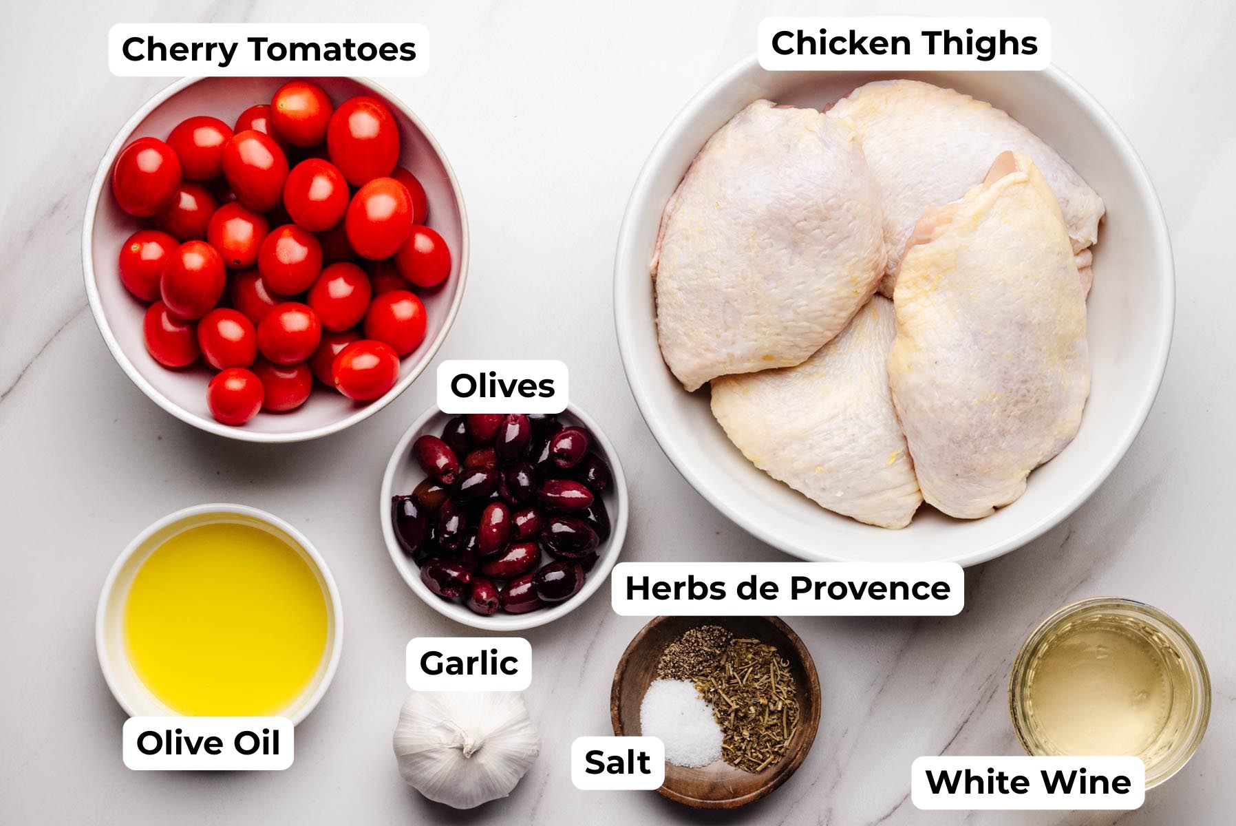 Labeled ingredients for Proven&ccedil;al chicken including chicken thighs, cherry tomatoes, olives, garlic, olive oil, white wine, salt, and Herbs de Provence.