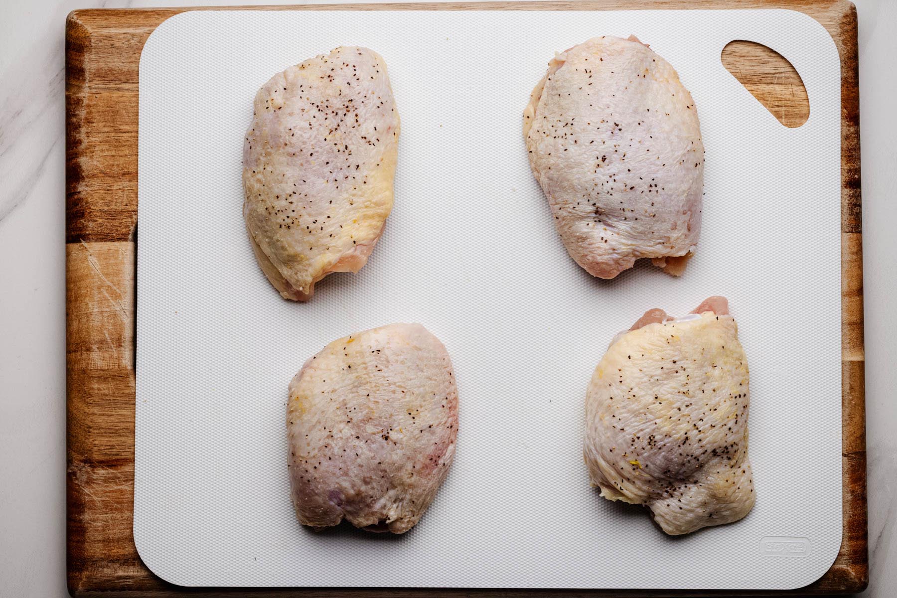 Raw chicken thighs seasoned with salt and pepper on a cutting board before cooking.