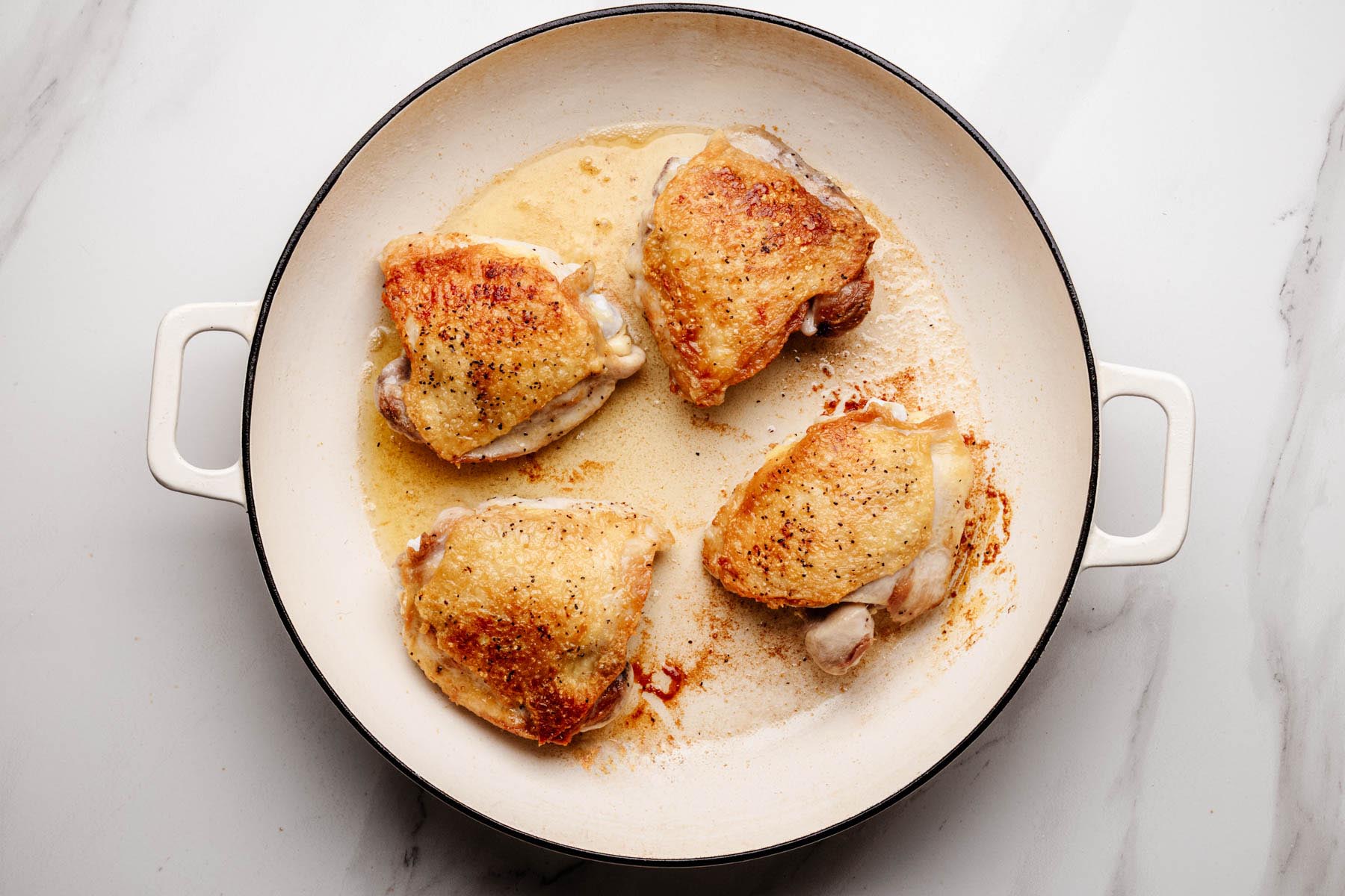 Chicken thighs browning skin-side down in a large white skillet.