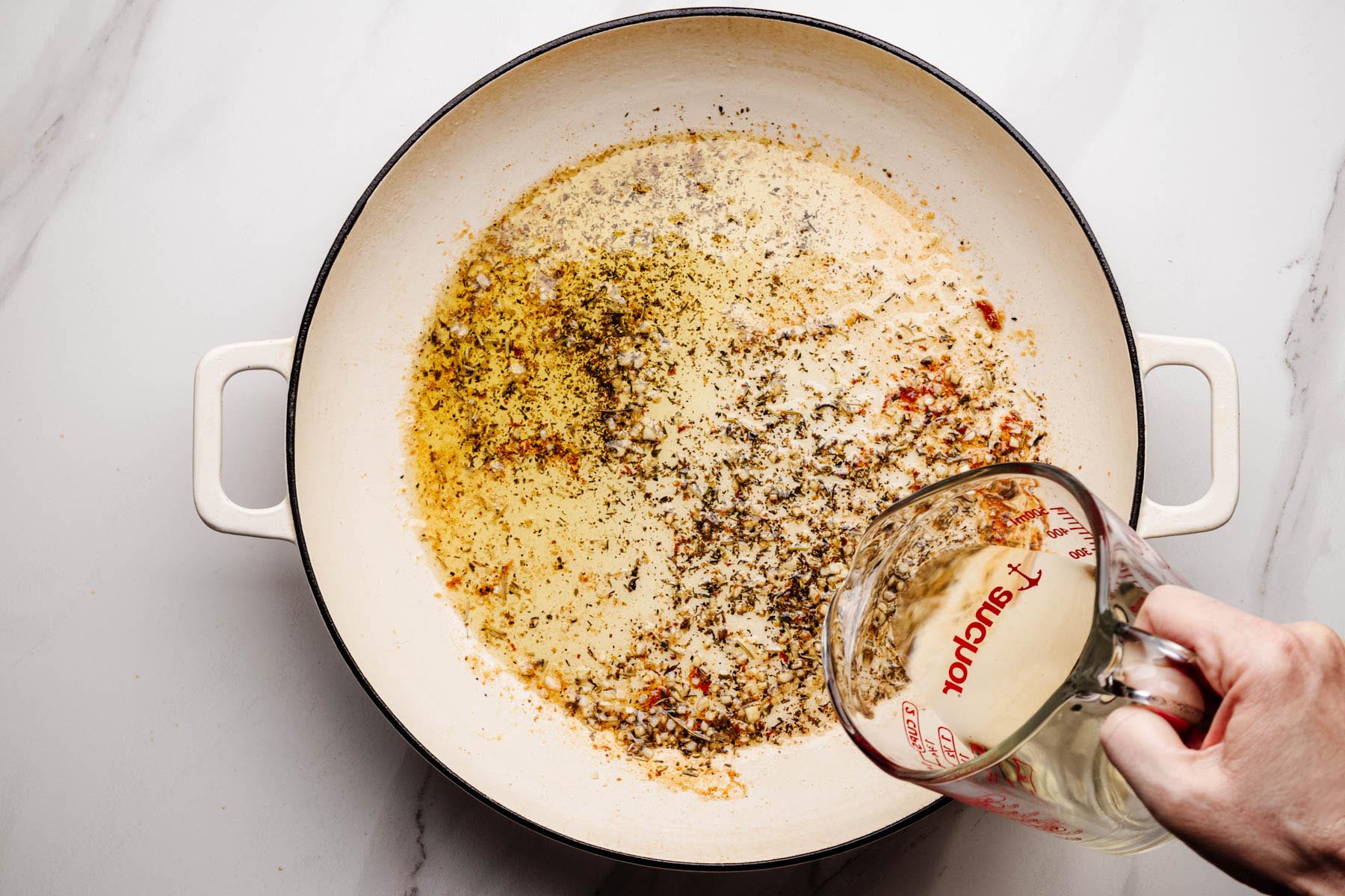 White wine being poured into the skillet with garlic and herbs to deglaze the pan.