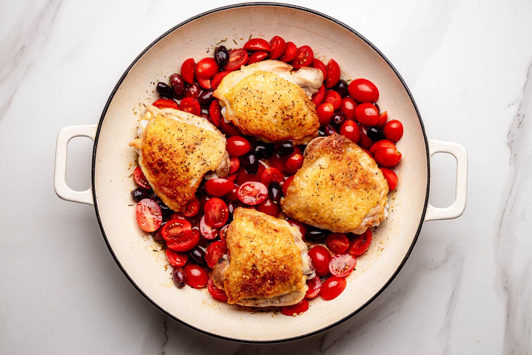 Chicken thighs simmering in a skillet with cherry tomatoes and olives for Chicken Proven&ccedil;al.