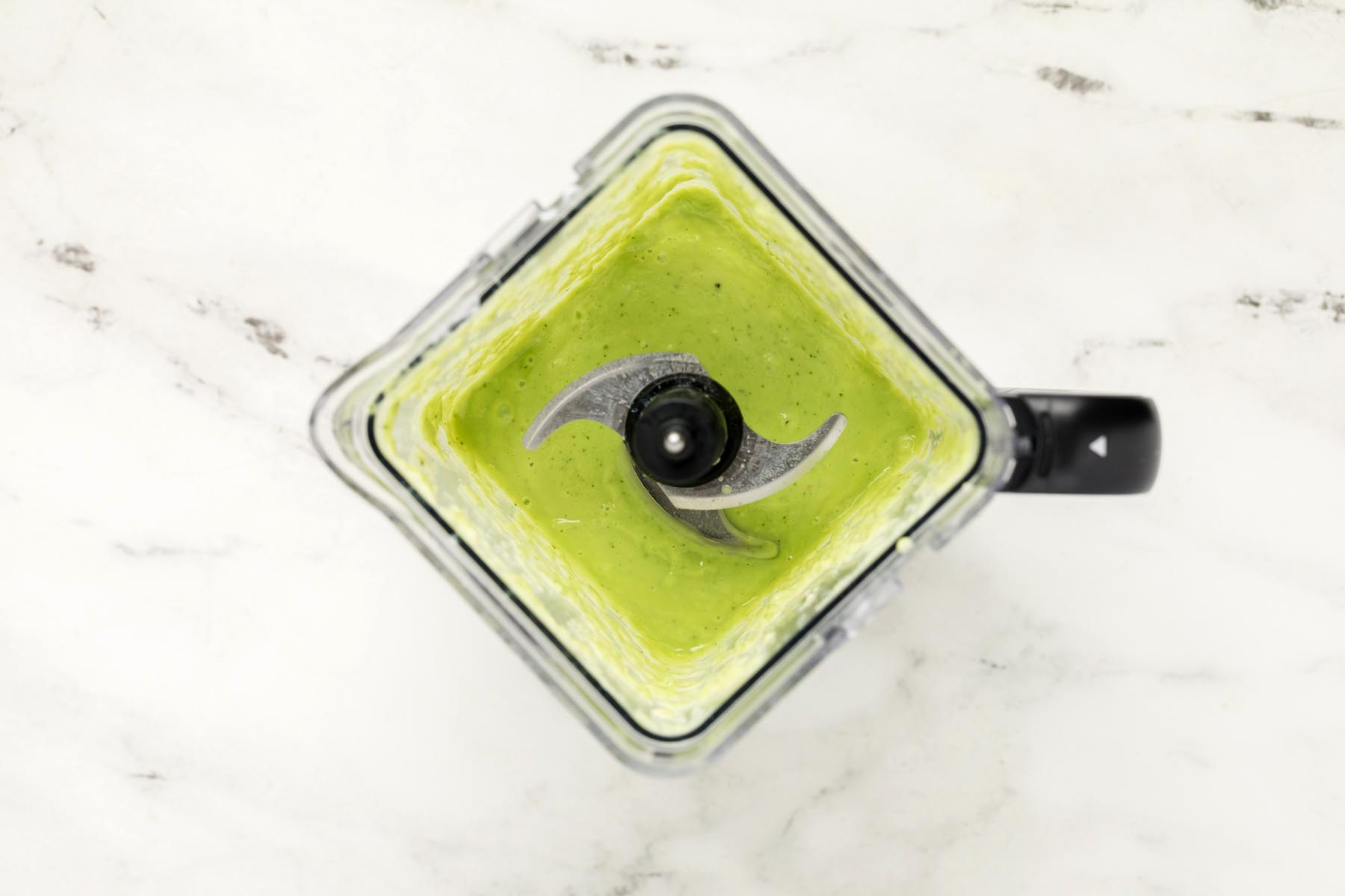Overhead view of blended gazpacho soup in a blender with a smooth, creamy pale green texture.