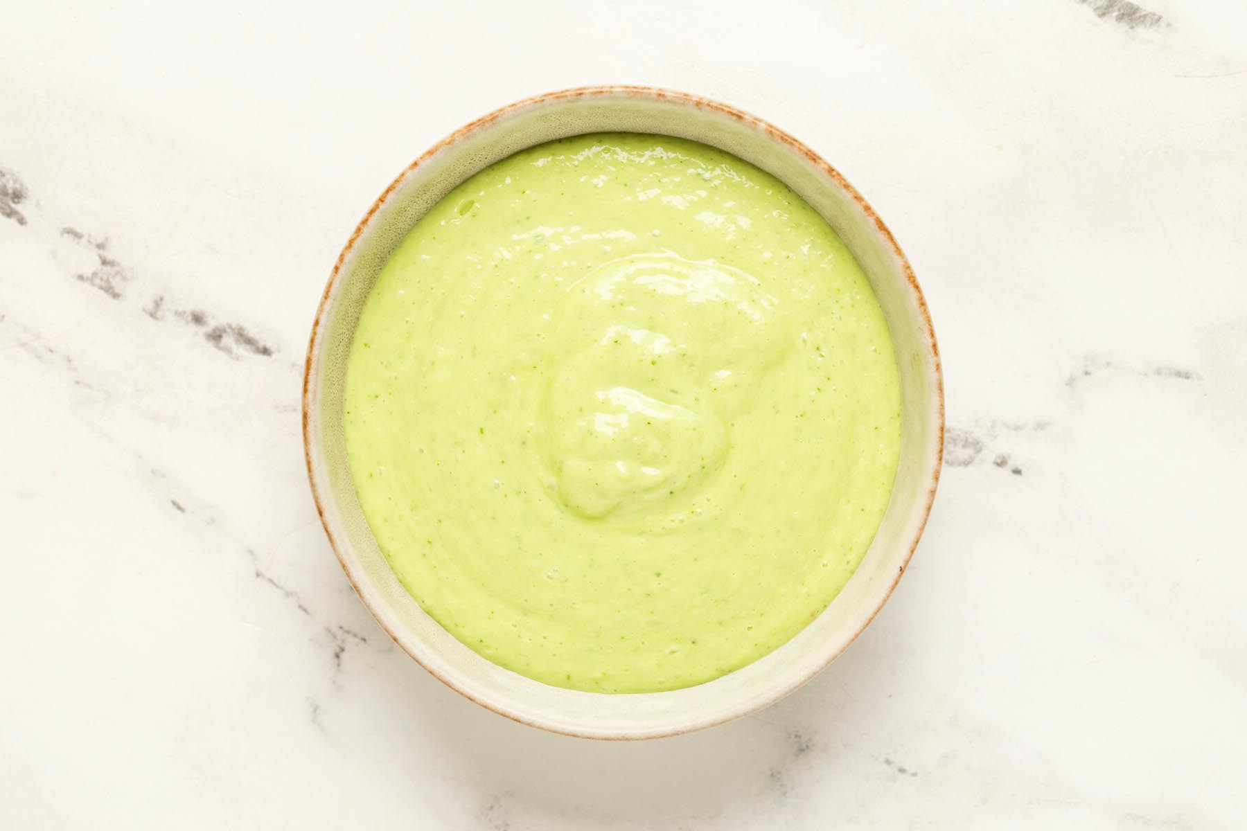 Overhead view of plain cucumber gazpacho in a beige bowl before adding toppings.
