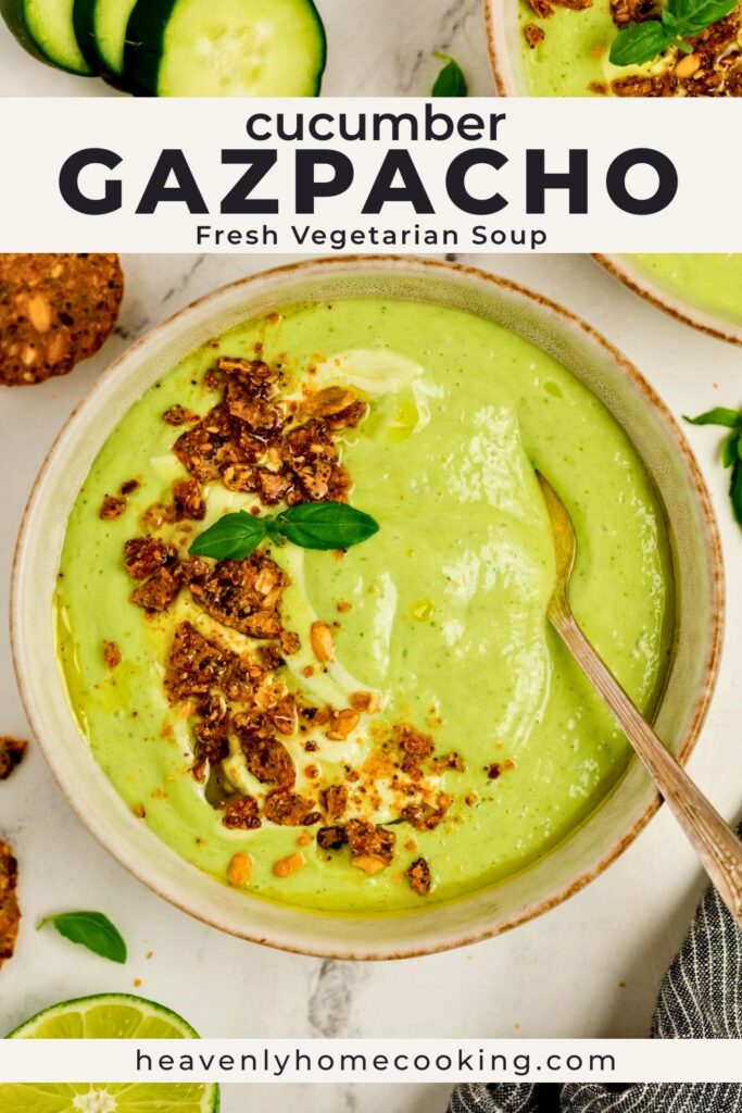 Creamy cucumber gazpacho topped with crunchy garnish, olive oil, and fresh basil in a ceramic bowl with a spoon. Vertical Pinterest pin for a fresh vegetarian cucumber gazpacho soup recipe from Heavenly Home Cooking.