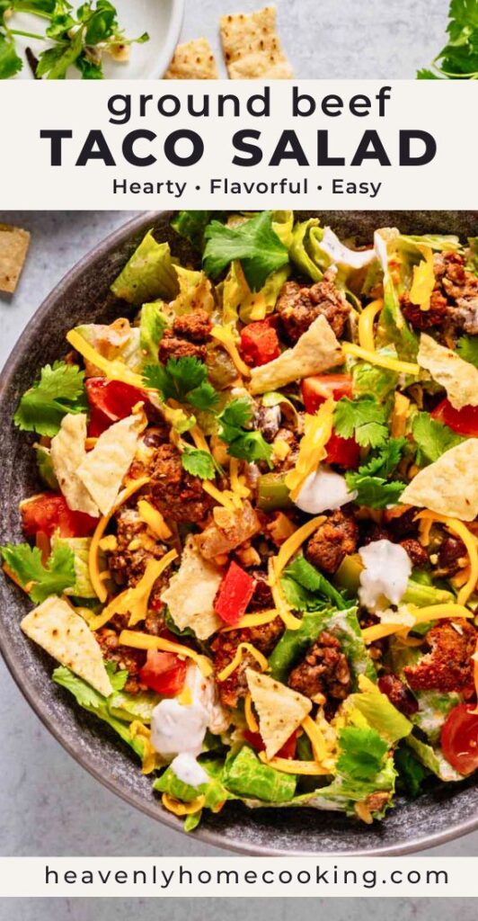 Ground beef taco salad loaded with seasoned beef, lettuce, tomatoes, cheddar cheese, tortilla chips, black beans, and cilantro in a dark bowl. Vertical Pinterest pin for an easy taco salad dinner recipe from Heavenly Home Cooking.
