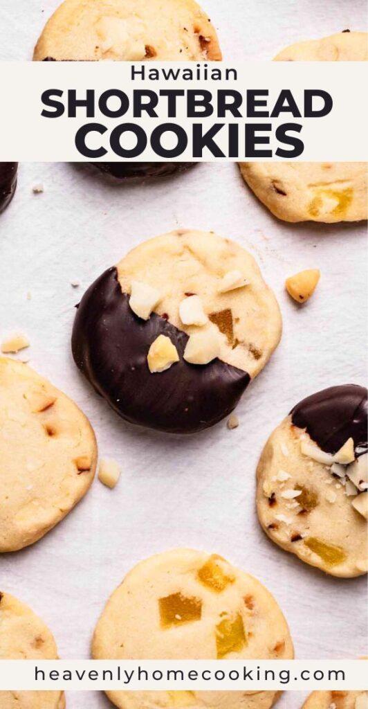 Hawaiian shortbread cookies with pineapple pieces and chocolate-dipped edges topped with macadamia nuts on a light surface. Vertical Pinterest pin for tropical homemade shortbread cookies from Heavenly Home Cooking.