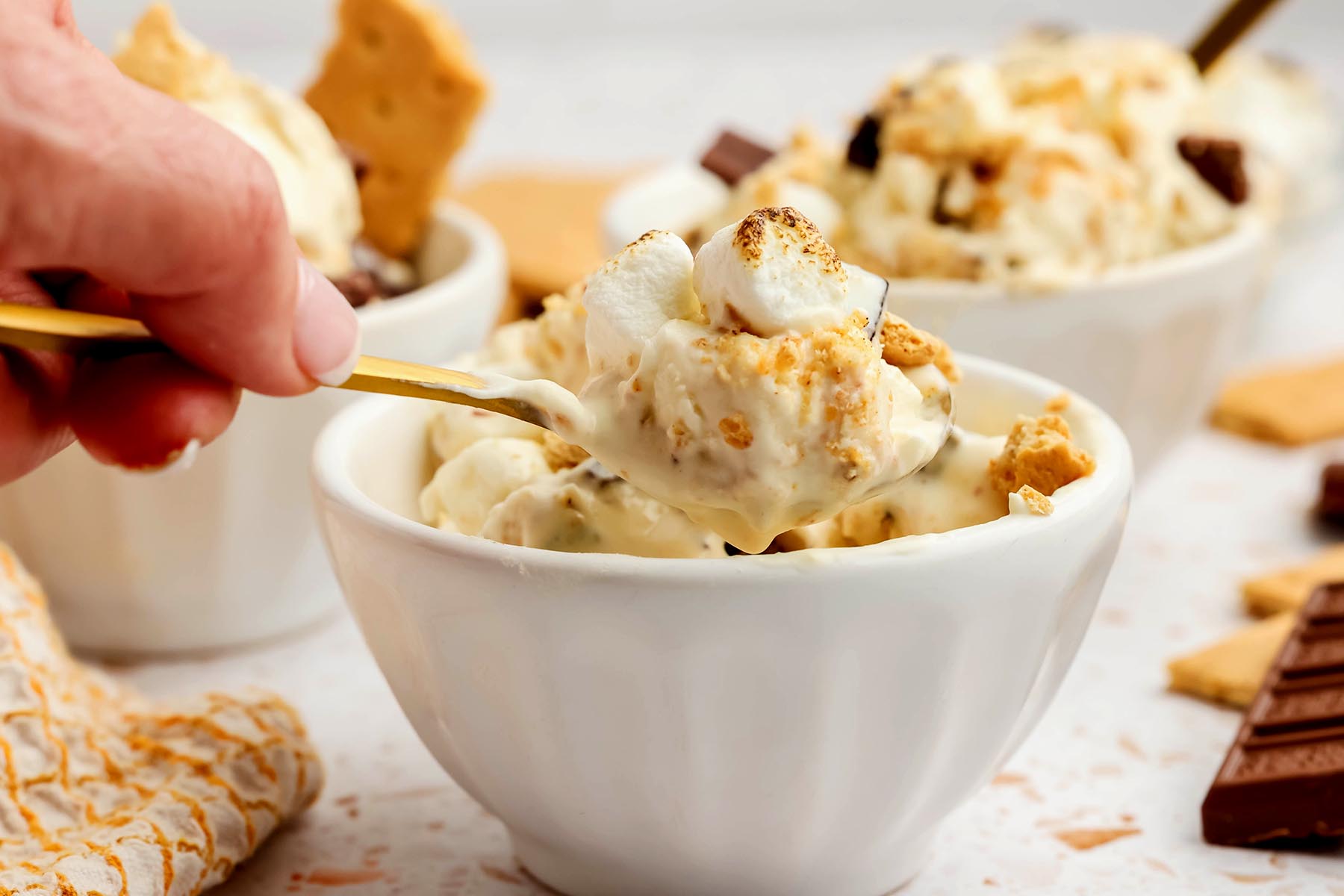 Hand holding a spoonful of homemade s’mores ice cream topped with mini marshmallows and graham crack
