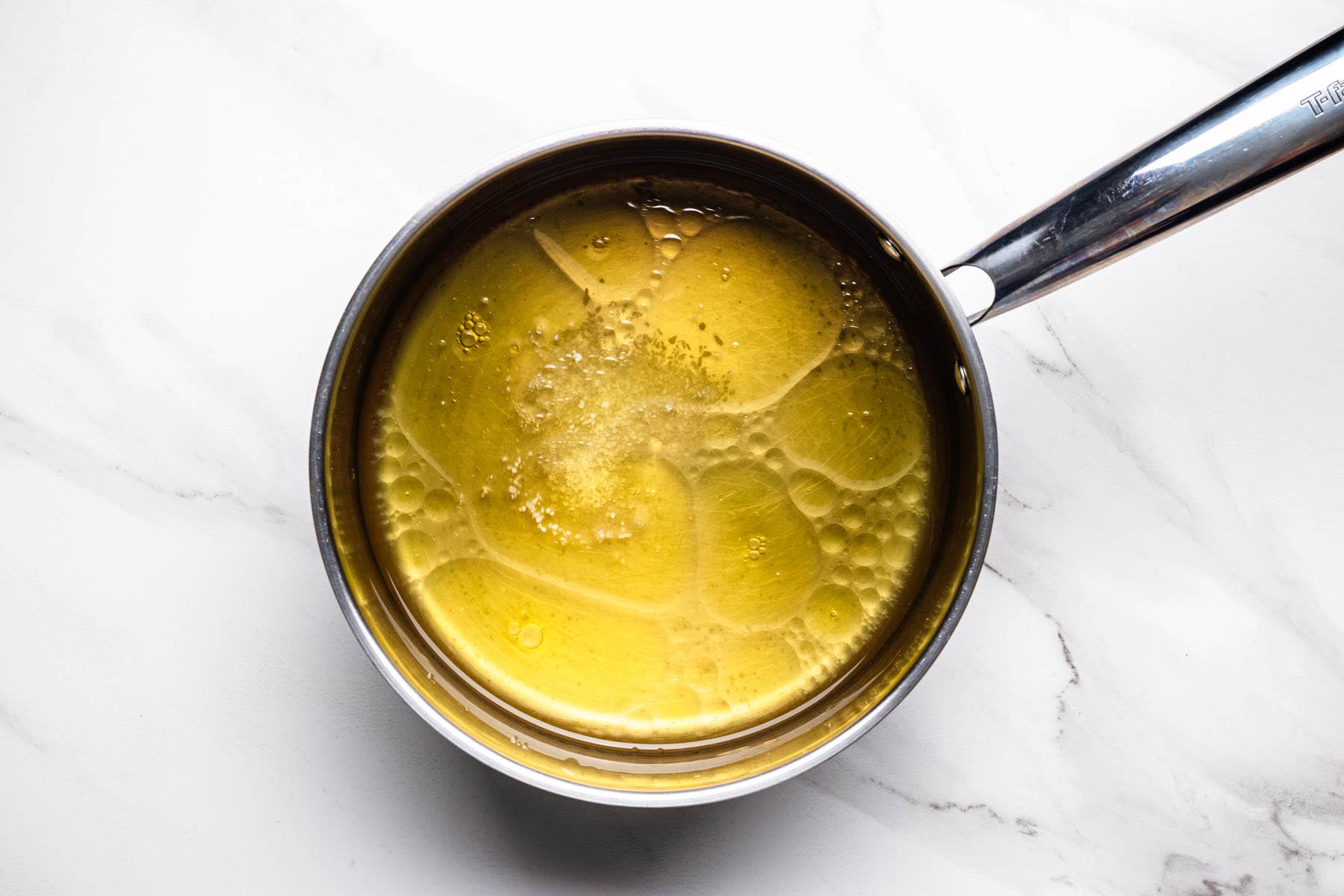 Chicken broth, olive oil, and salt heating together in a saucepan before bringing to a boil.