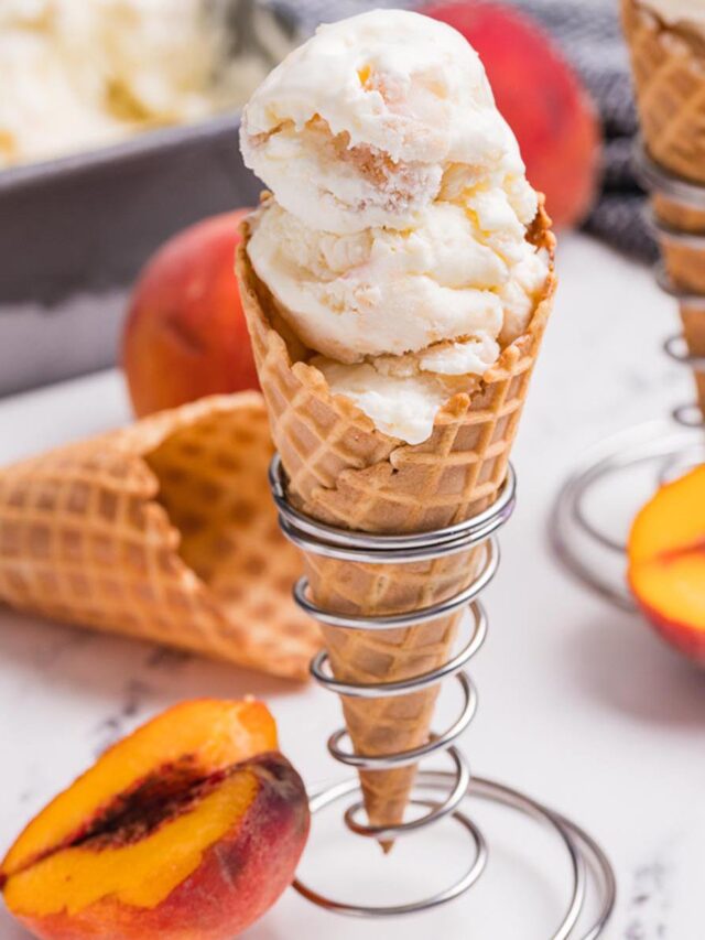 Homemade peach ice cream in a waffle cone with fresh peach slices and creamy frozen dessert in the background.