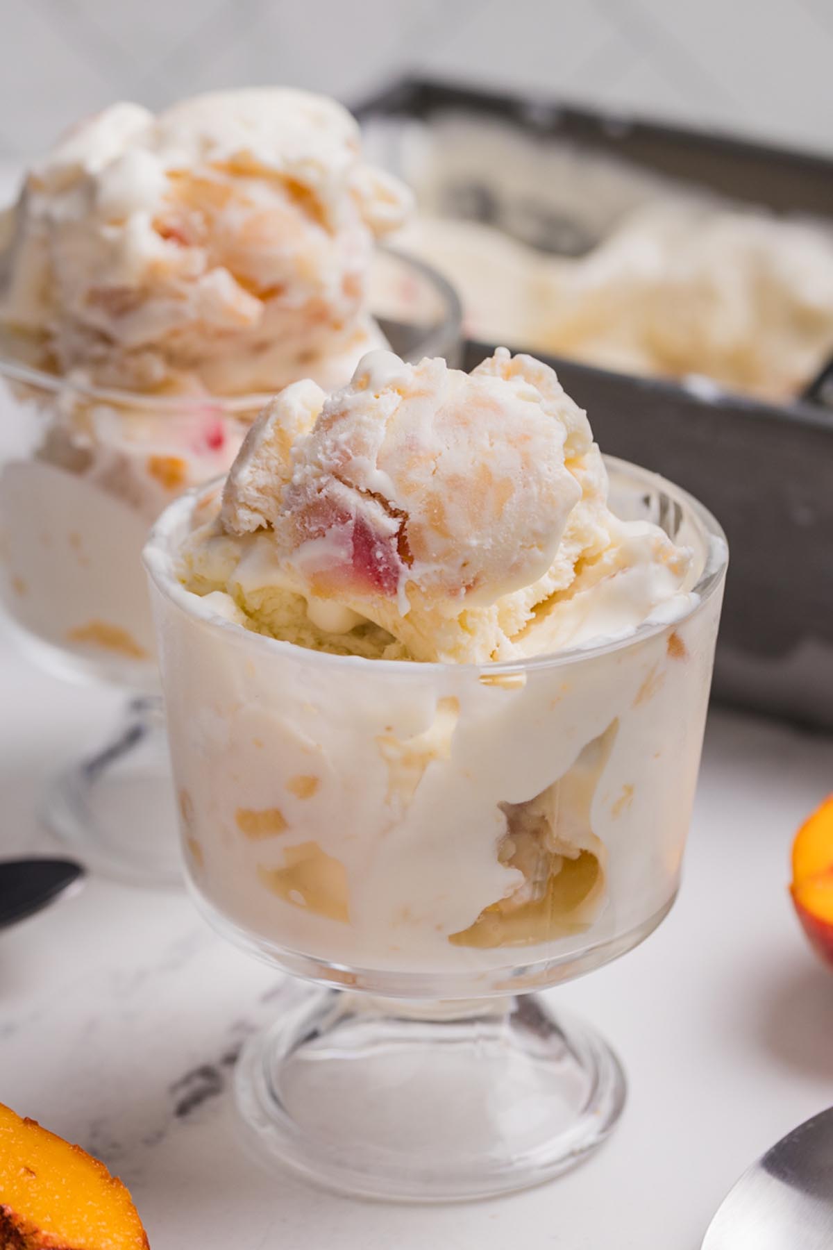 Peach ice cream served in a glass dessert dish with chunks of fresh peaches and a creamy no churn ice cream texture.