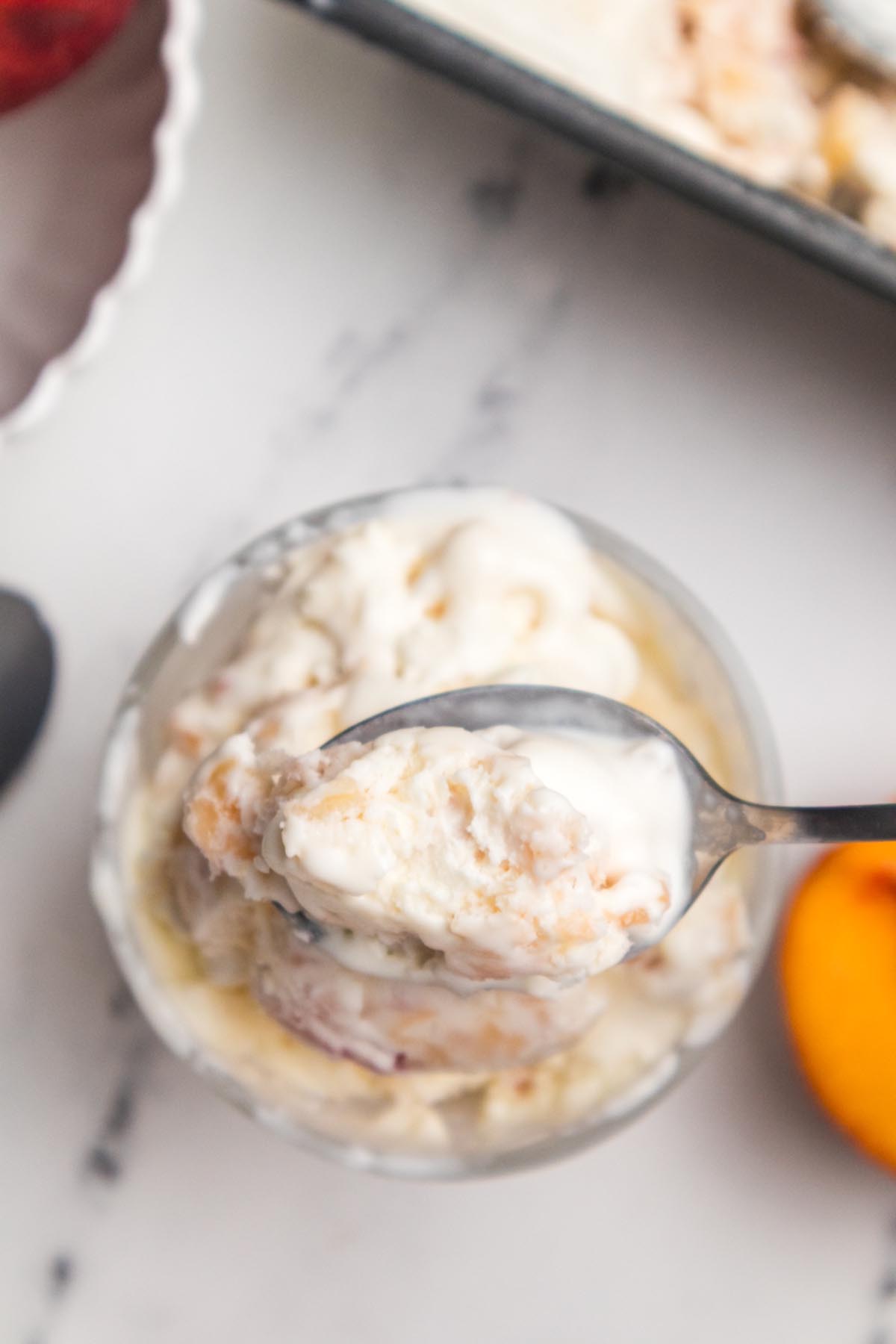 Spoonful of homemade peach ice cream with fresh peach pieces in a creamy summer frozen dessert.