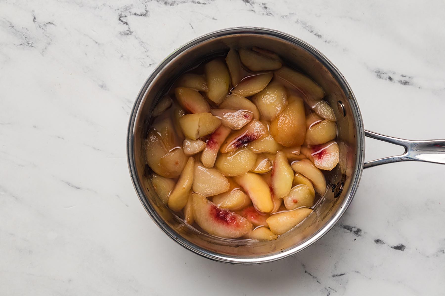 Fresh peaches simmering in a saucepan to make peach puree for creamy no churn ice cream.