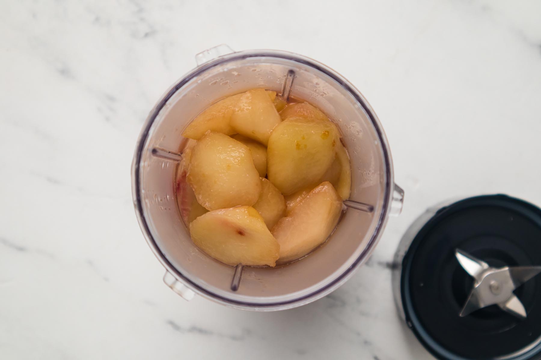 Cooked peach mixture in a blender cup before blending for homemade peach frozen dessert.