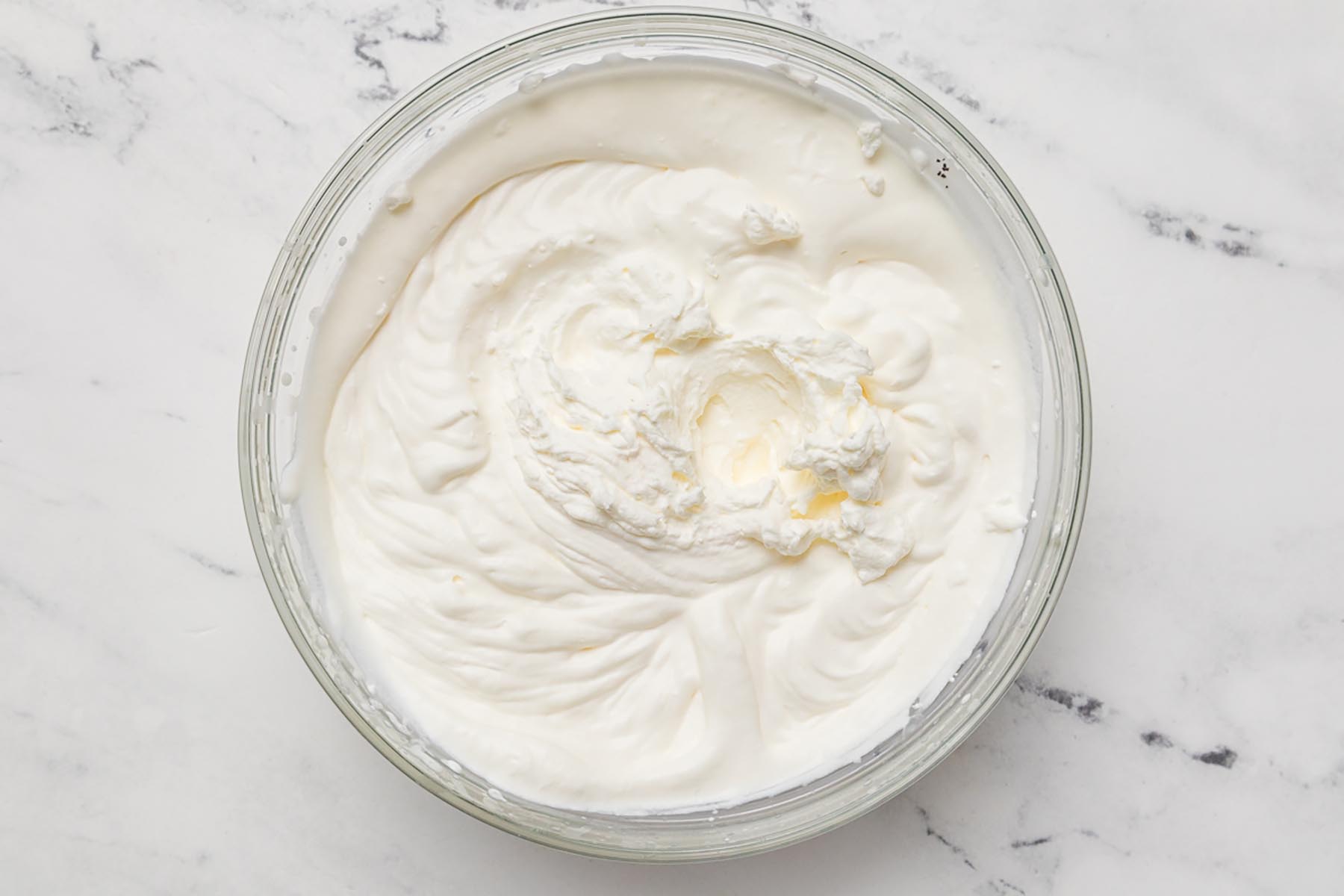 Fresh whipped cream beaten to stiff peaks for homemade no churn vanilla peach ice cream.