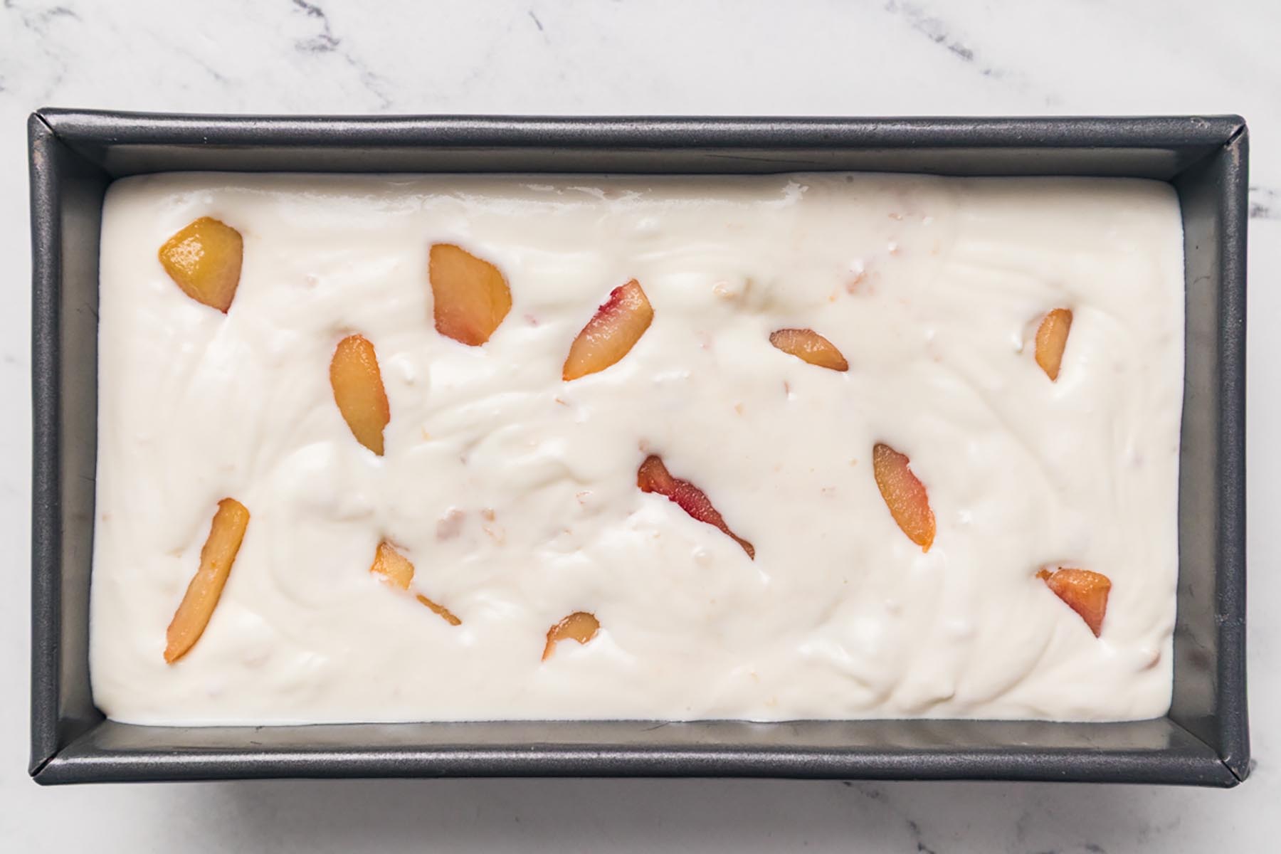 Peach ice cream mixture spread into a loaf pan with peach pieces on top before freezing overnight.