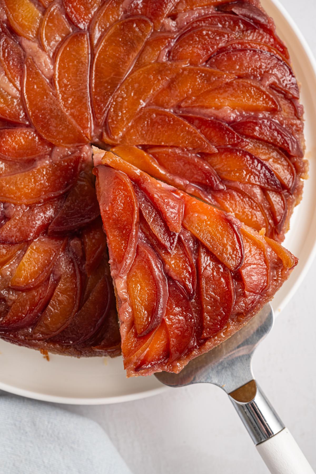 Close-up of peach upside down cake with a slice being removed on a cake server, showing glossy peaches and caramelized topping.