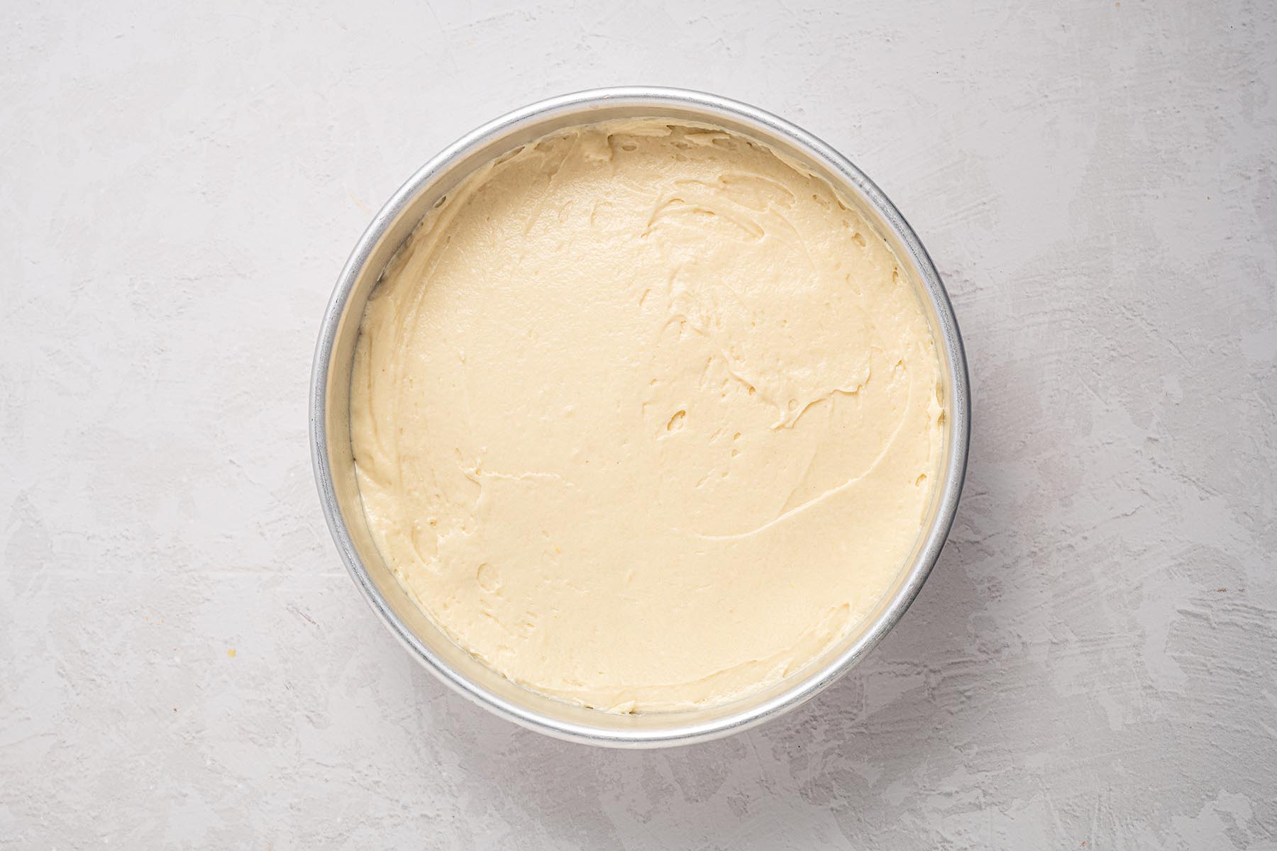 Batter spread evenly over sliced peaches in a round cake pan before baking.