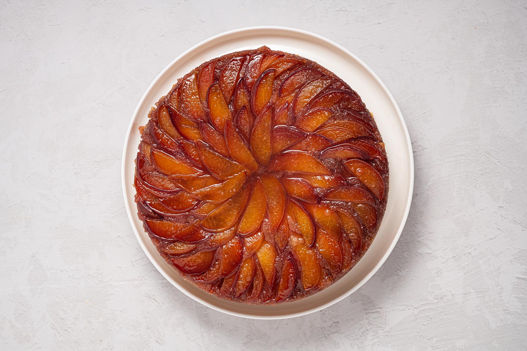 Peach upside down cake inverted onto a serving plate with caramelized peaches on top.
