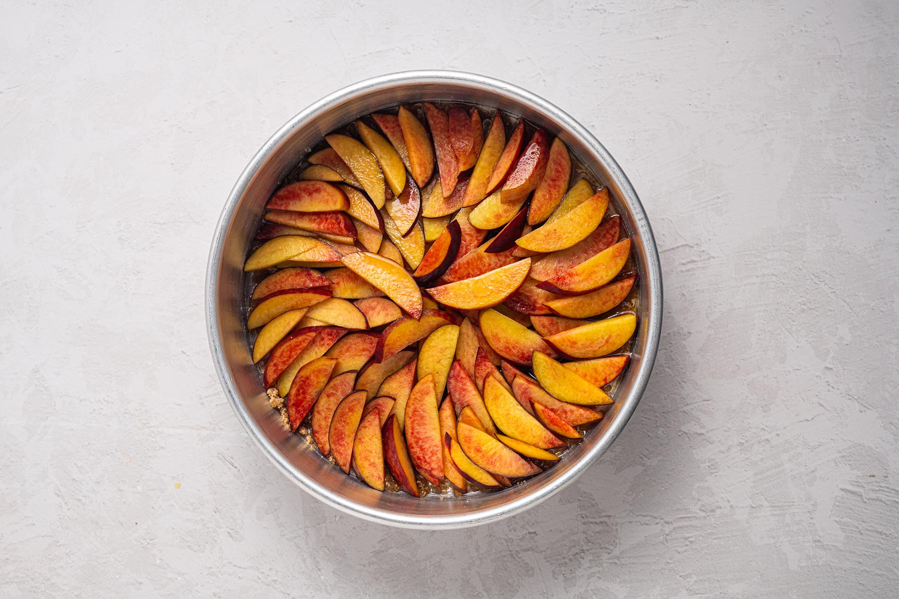 Peach slices arranged in a circular pattern in a round cake pan for an upside down peach cake.