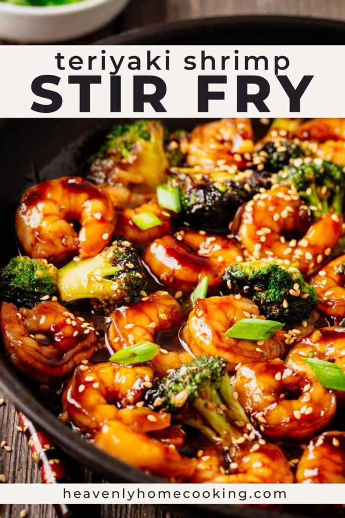 Close-up teriyaki shrimp stir fry with glossy shrimp, broccoli florets, sesame seeds, and green onions in a black skillet with rich teriyaki sauce. Vertical Pinterest pin for a teriyaki shrimp stir fry recipe from Heavenly Home Cooking.