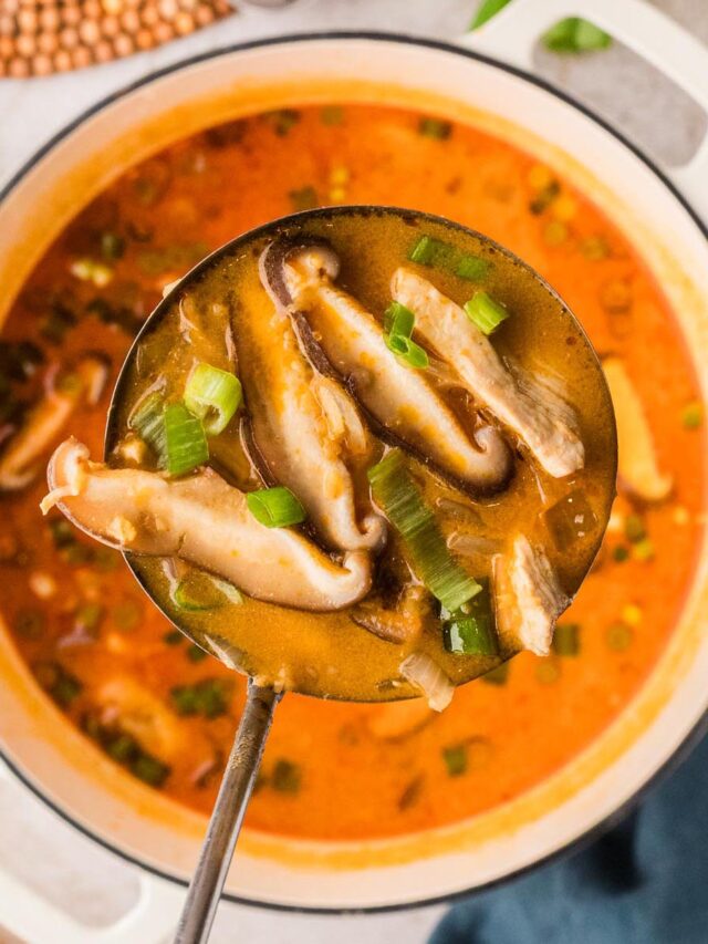 Thai chicken soup with red curry and coconut milk in a white Dutch oven, topped with green onions and mushrooms