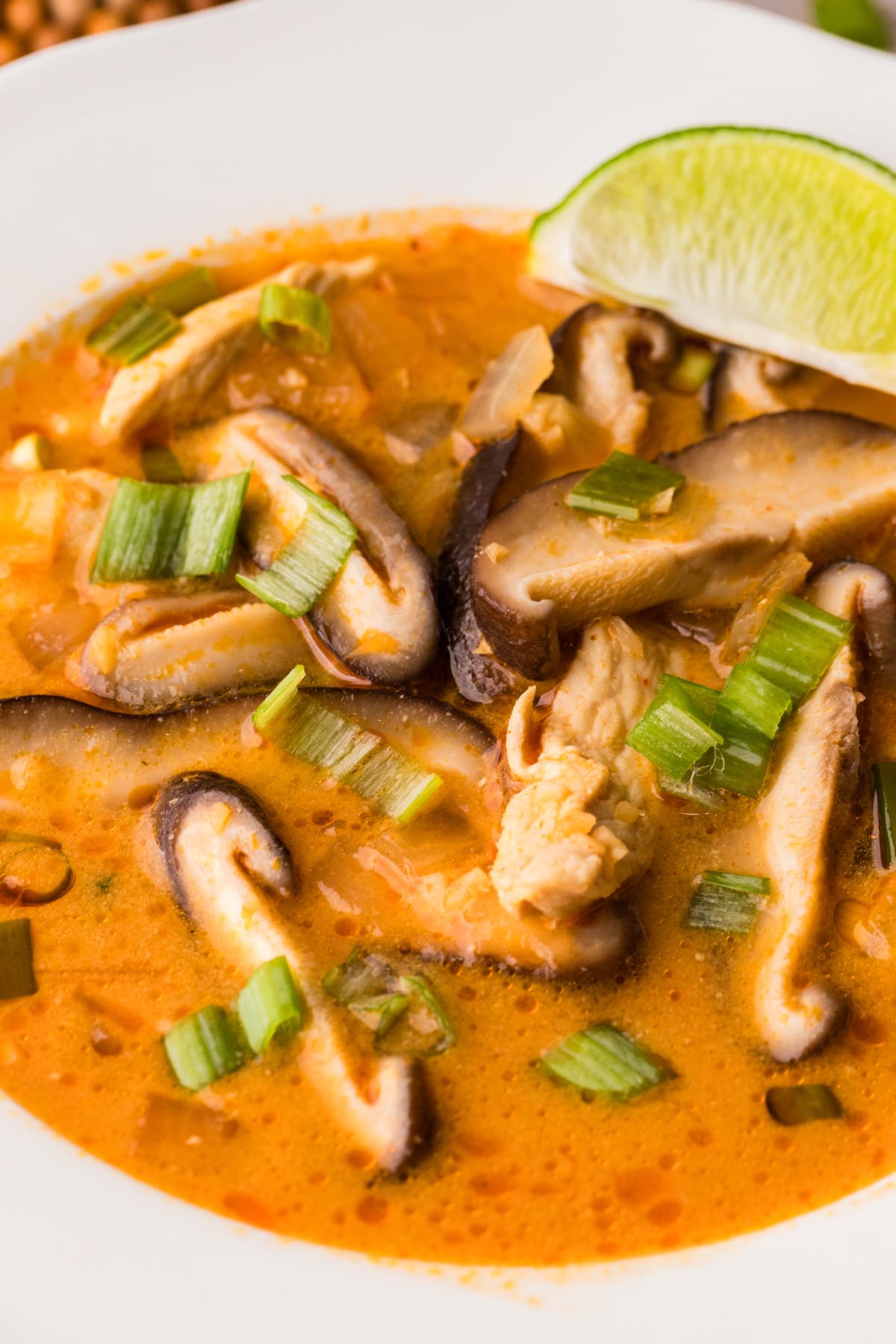 Creamy Thai coconut chicken soup with mushrooms, green onions, and fresh lime wedge.