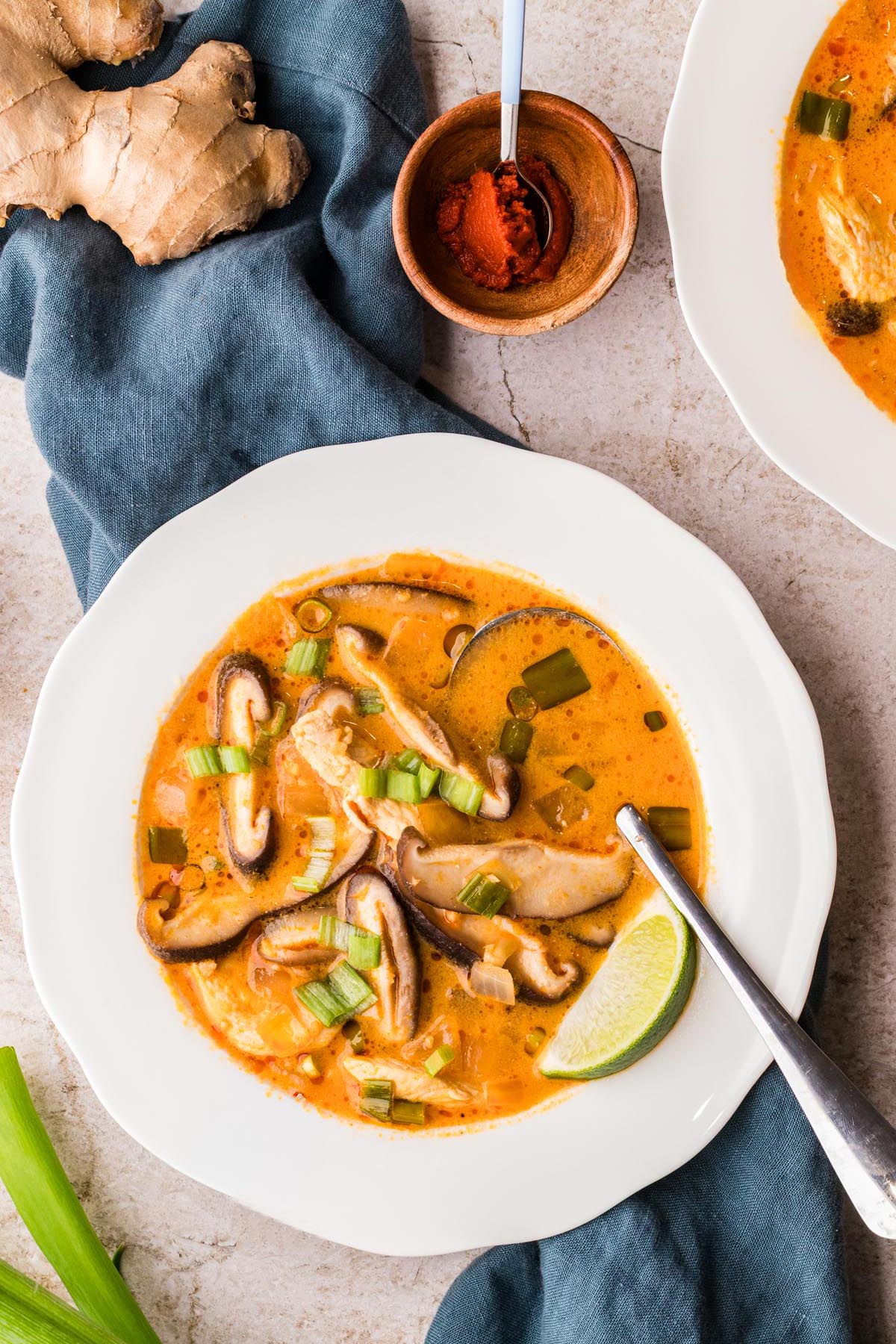 Thai-style coconut chicken soup served in a white wide brimmed soup bowl with mushrooms, green onions, and lime