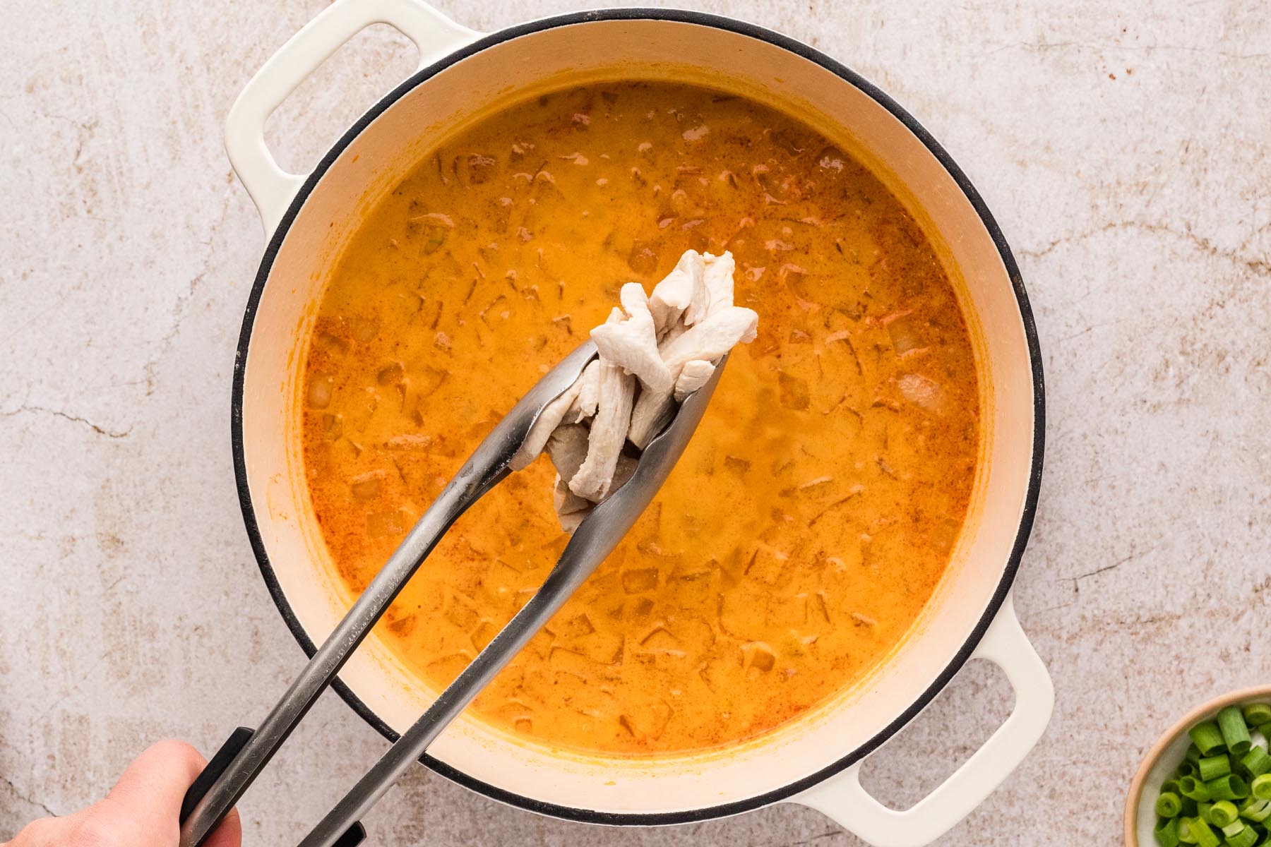 Cooked chicken being added with tongs back into Thai curry broth.