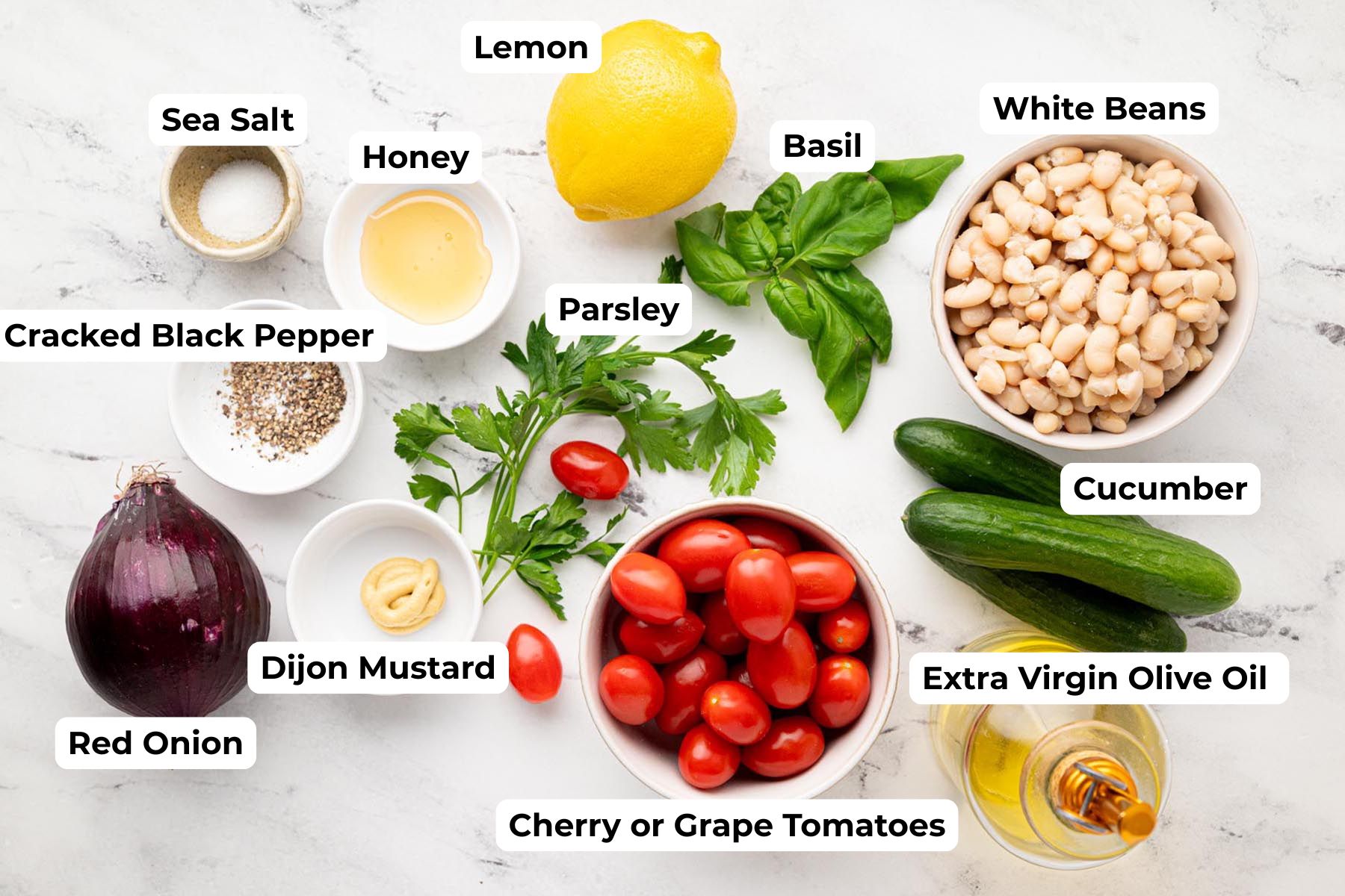 Ingredients for Mediterranean white bean salad including white beans, cherry tomatoes, cucumber, red onion, parsley, basil, lemon, olive oil, Dijon mustard, honey, sea salt, and black pepper.