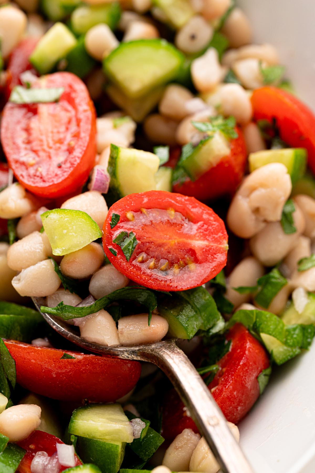 Close-up of white bean salad with cherry tomatoes, cucumber, parsley, and lemon vinaigrette on a spoon.